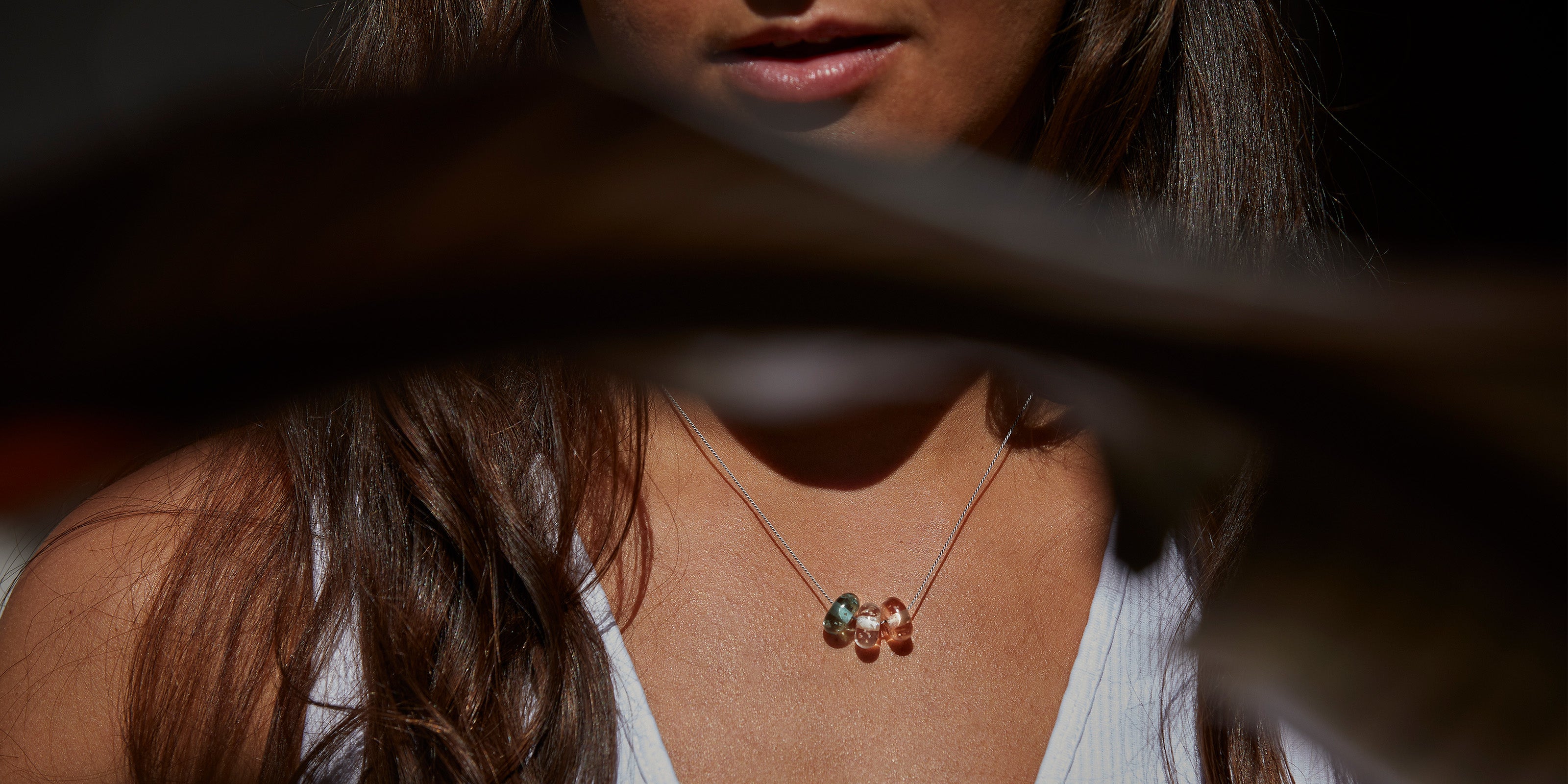 Pink, clear and grey small glass beads on fine silk cord necklace, worn by woman with long dark hair.