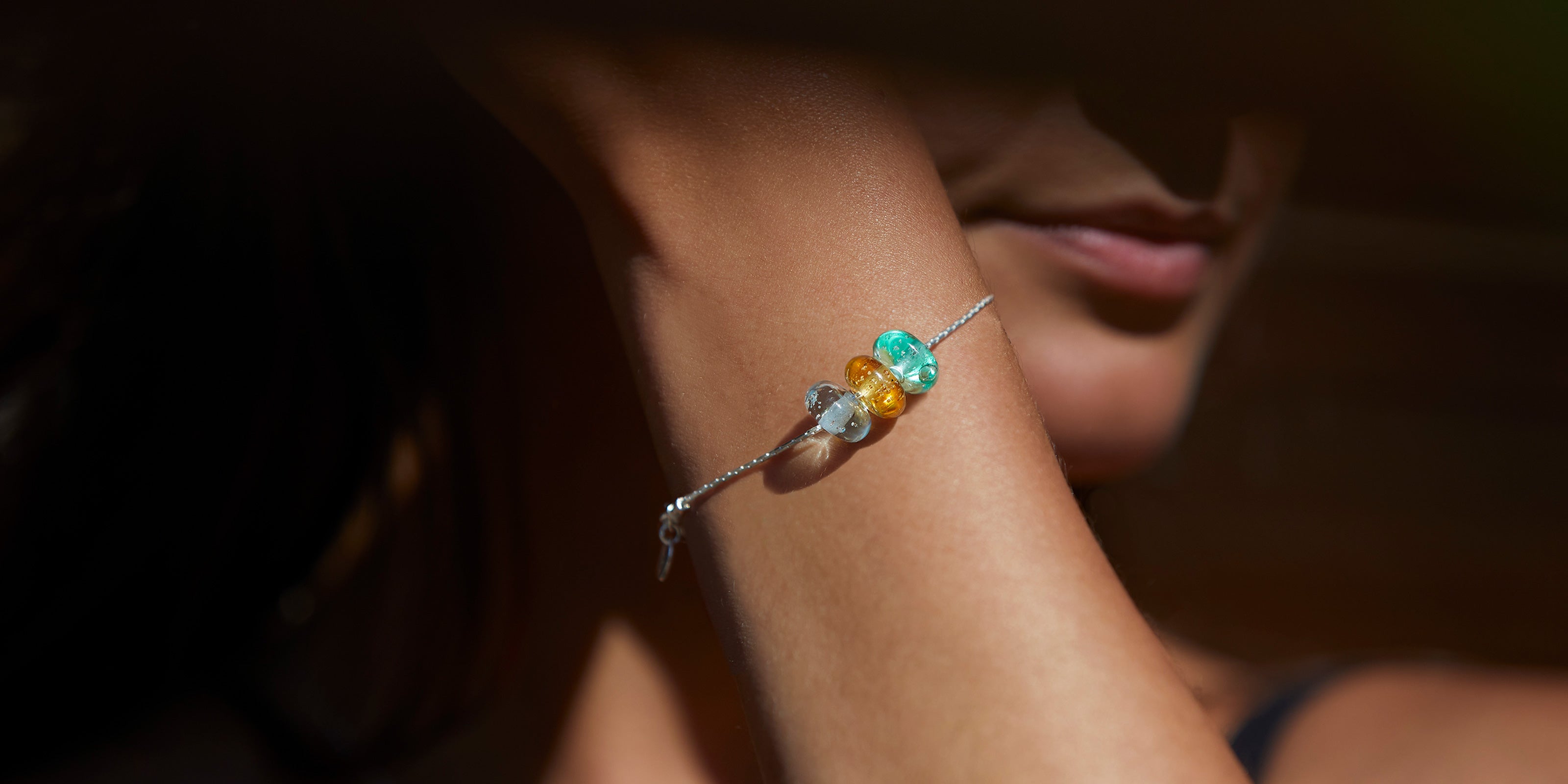 Blue, green and amber beach sand beads worn on sterling silver fine chain bracelet. Worn by girl.