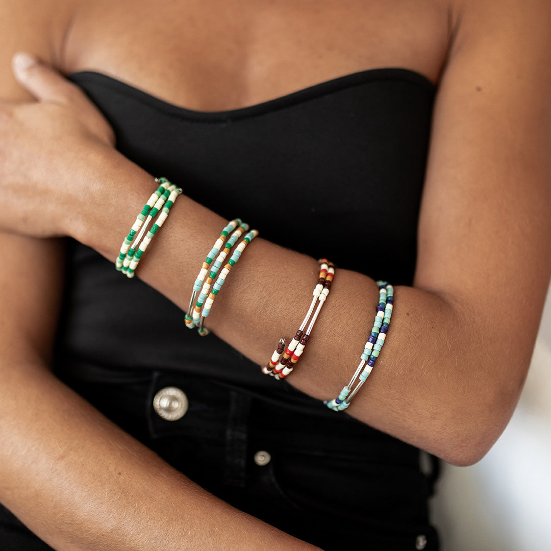 Person wearing colorful beaded bracelets on arms crossed.