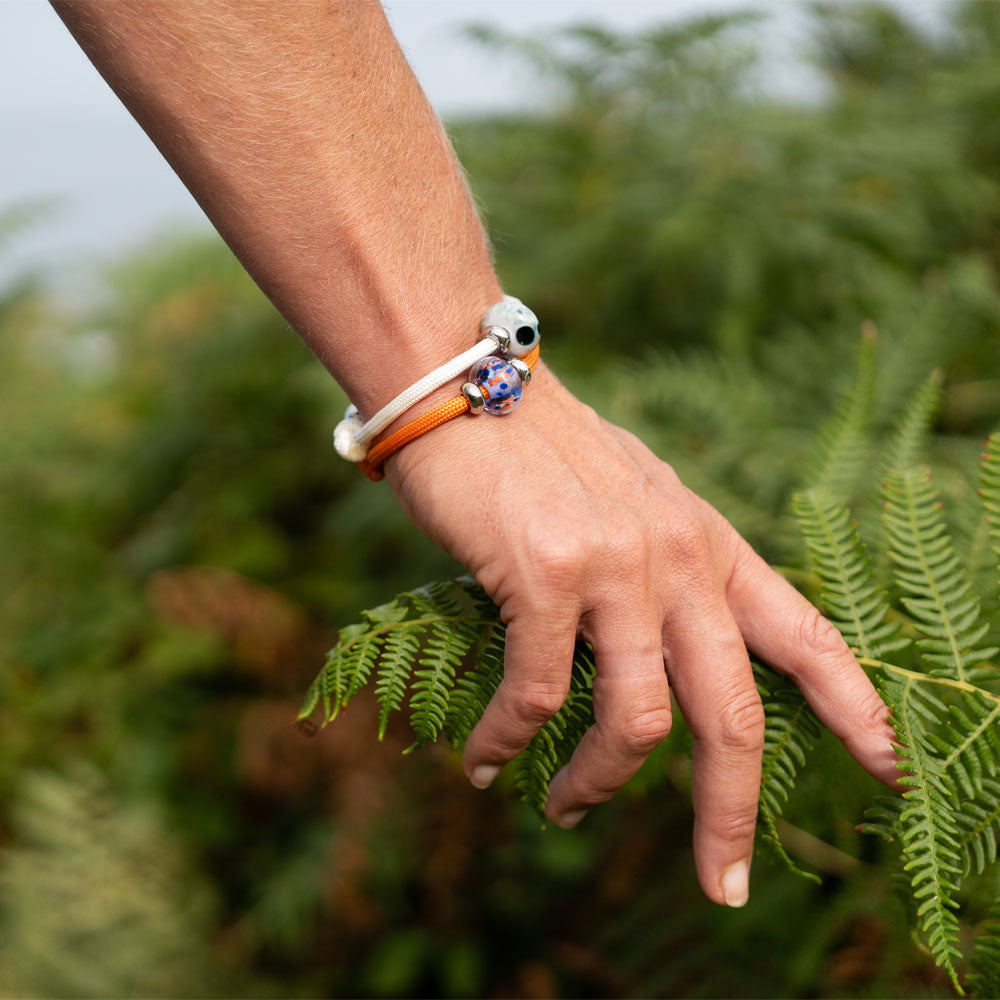 Hand wearing colorful bracelets holding a fern leaf with a blurred green background
