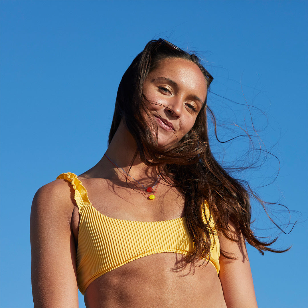 Dark haired woman wearing a yellow bikini top wearing red and yellow glass bead necklaces.