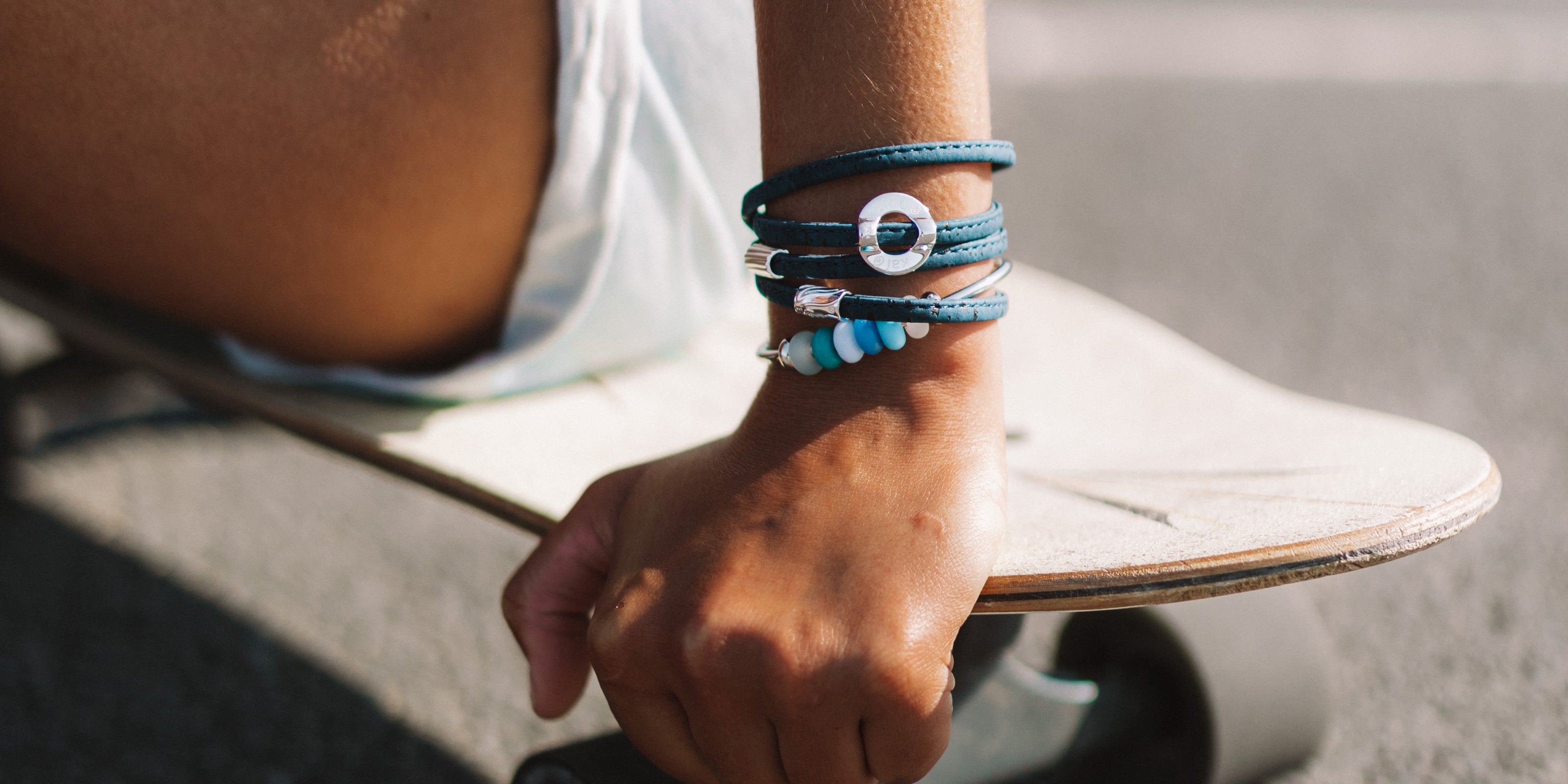Navy blue cork wrap bracelet with silver beads and colourful beads on bangle, sitting on skateboard.