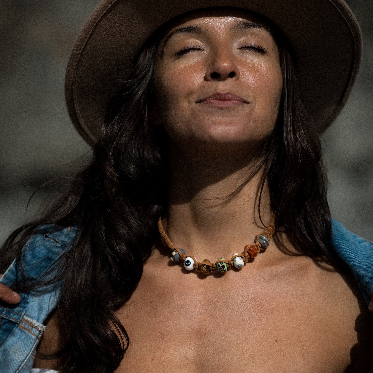 Woman with dark hair wearing a denim jacket and hat with a macrame braided brown cord necklace with glass beads raising money for the WWF.