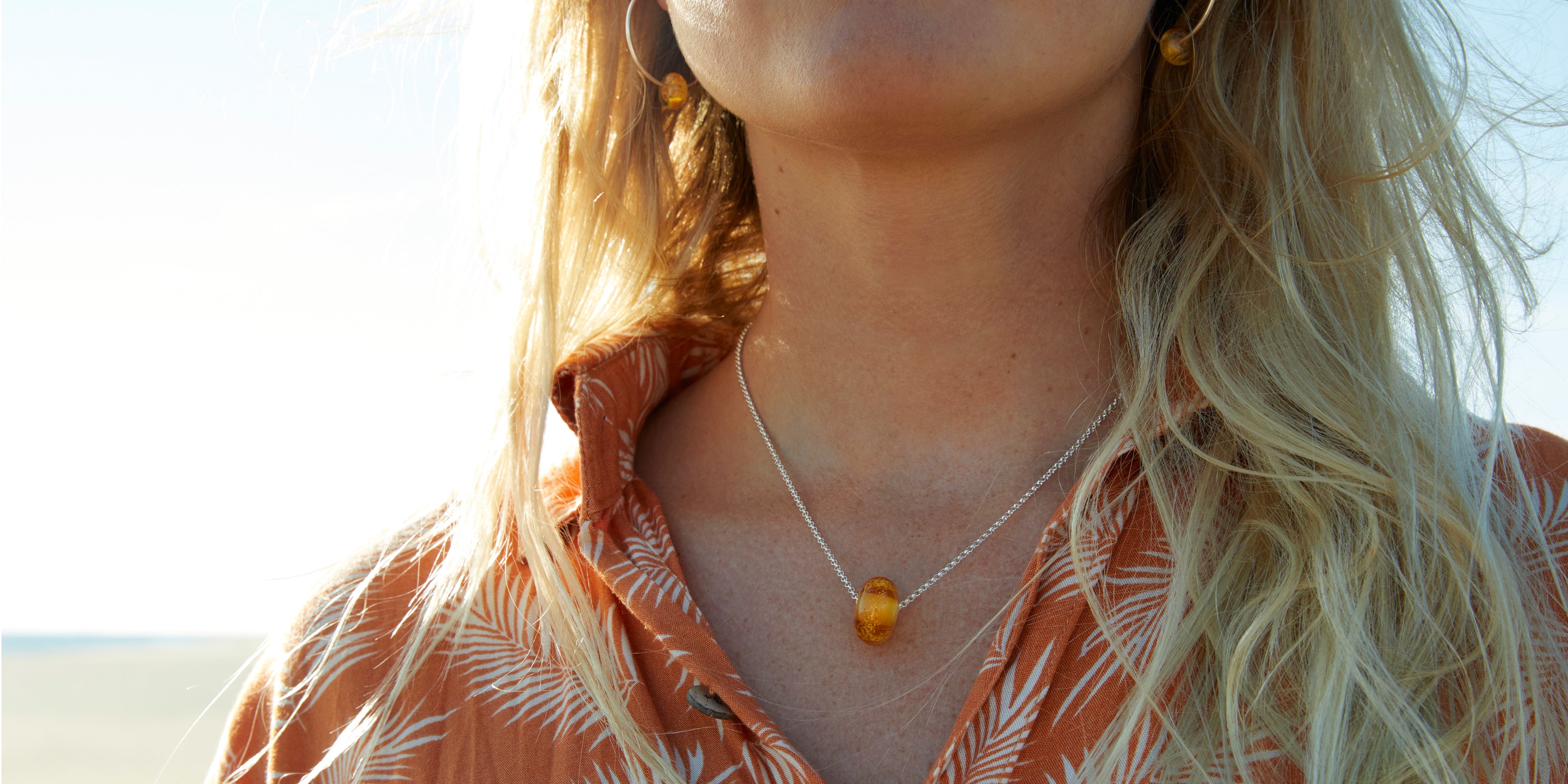 Girl on beach wearing amber glass sand bead necklace and earrings.
