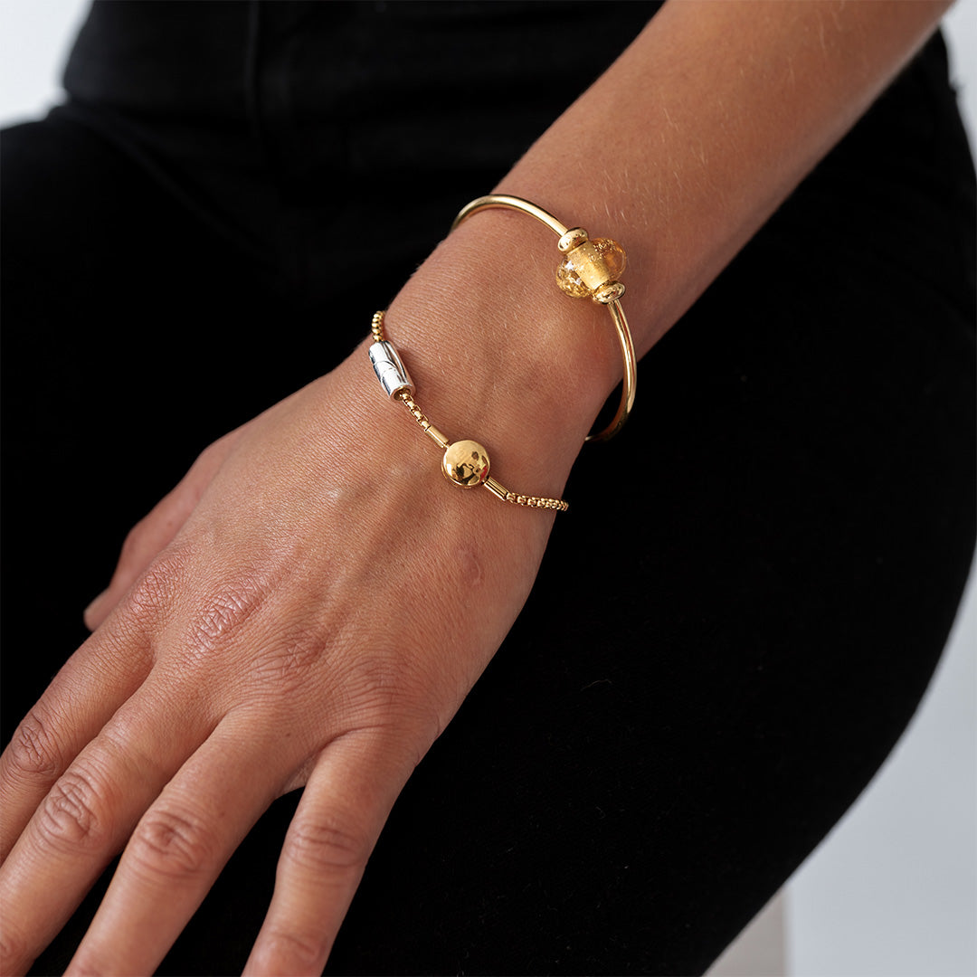 Person wearing a gold bangle and bracelet with amber glass sand bead.