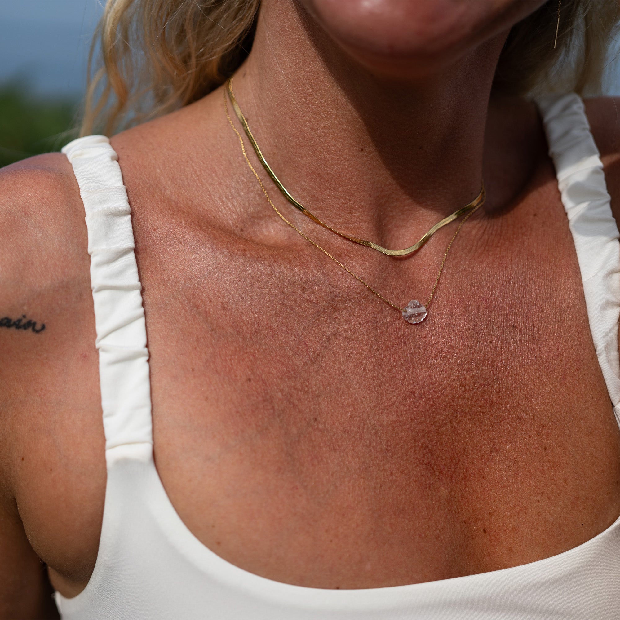 Close-up of a person wearing a gold necklace with a small pendant, outdoors.