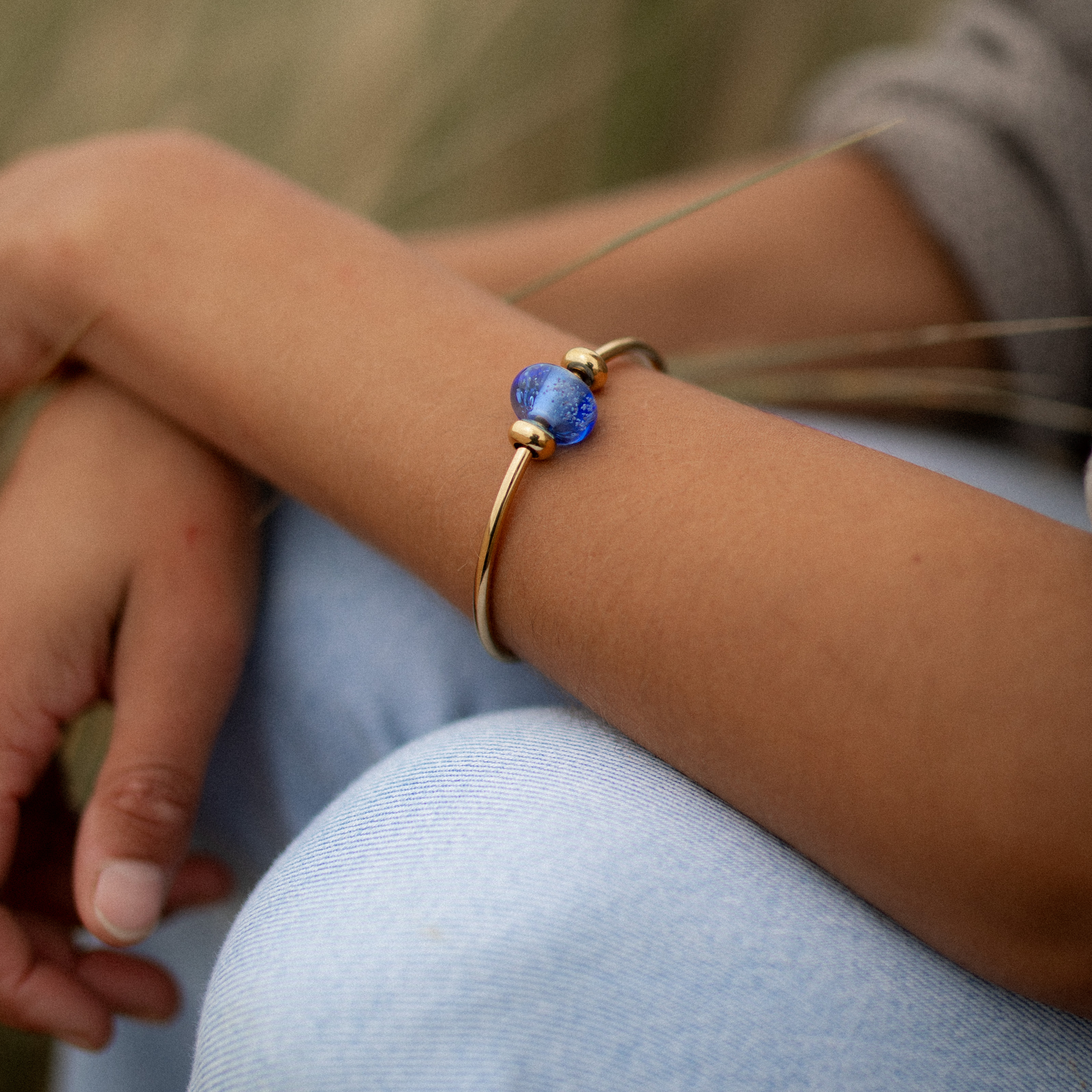 Person wearing gold bangle with blue glass bead.