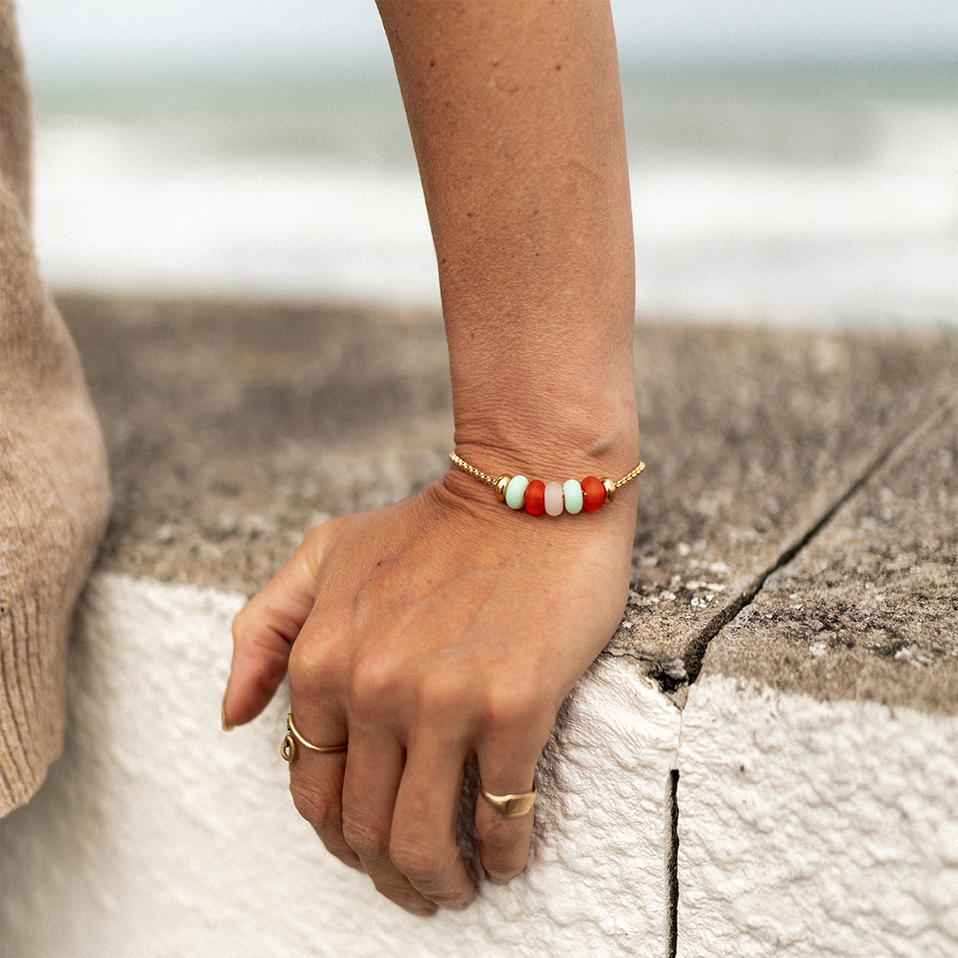 Gold Ula bracelet with blue and red glass baed worn by woman at the beach.