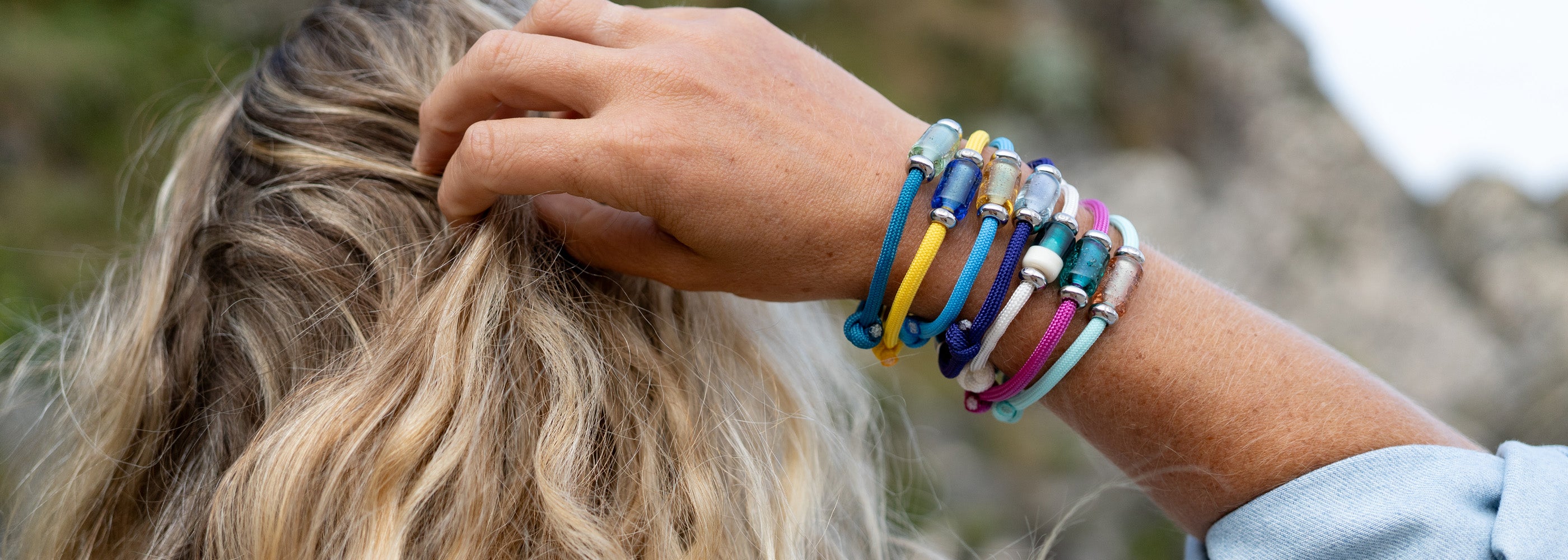 Person wearing colorful bracelets on a blurred natural background