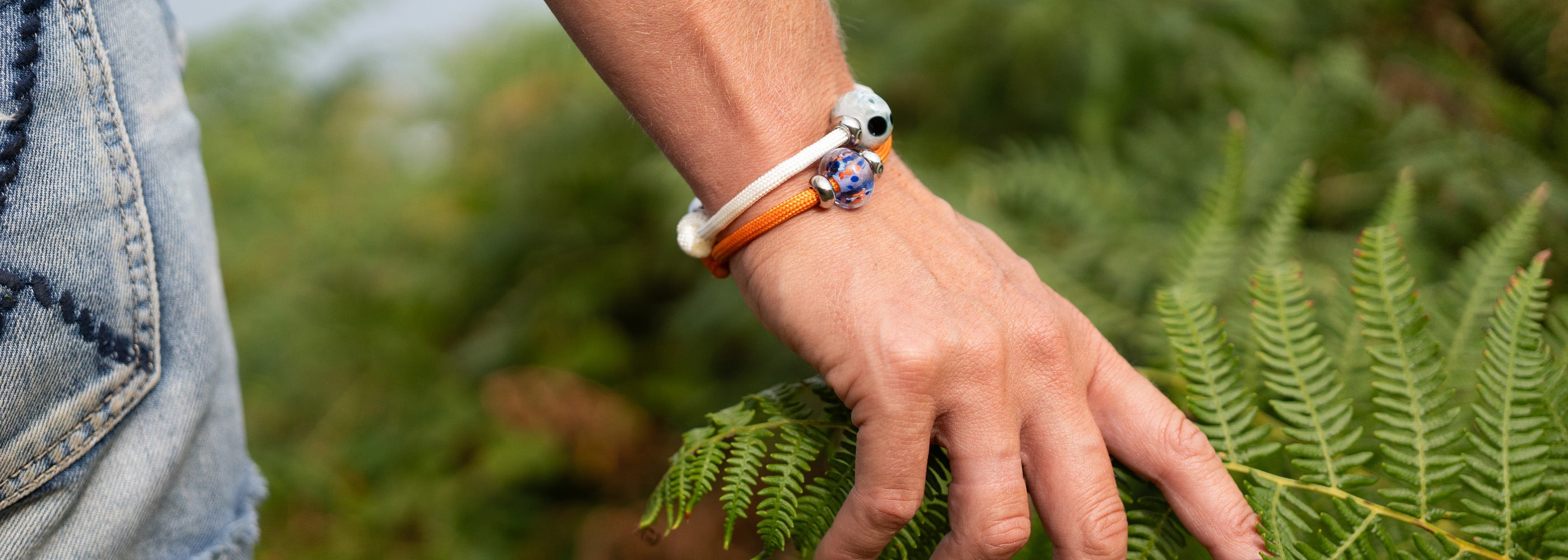 Hand with bracelets on a background of green ferns