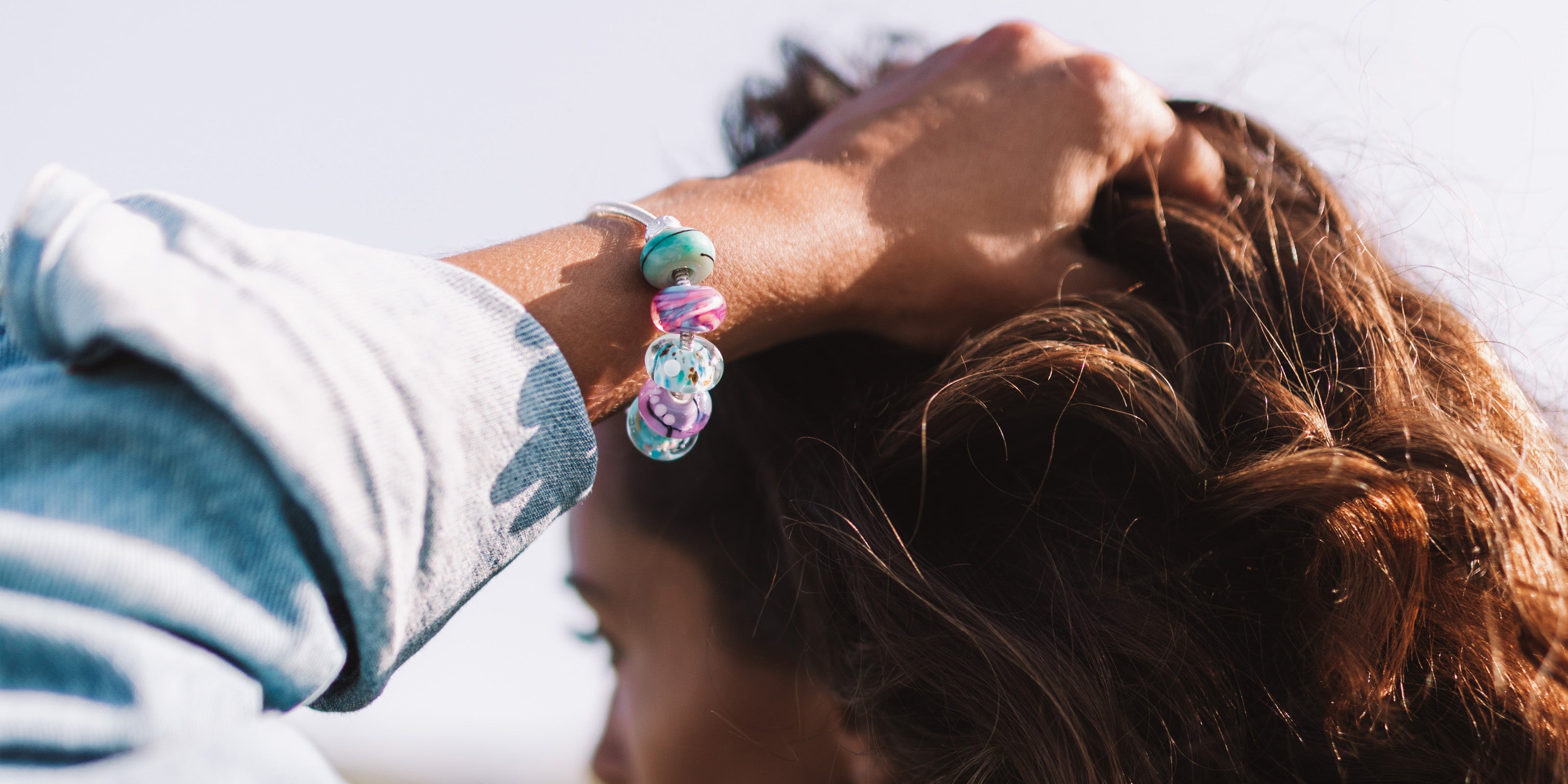 Blue, purple, green glass beads worn on silver bracelet by girl in denim jacket.