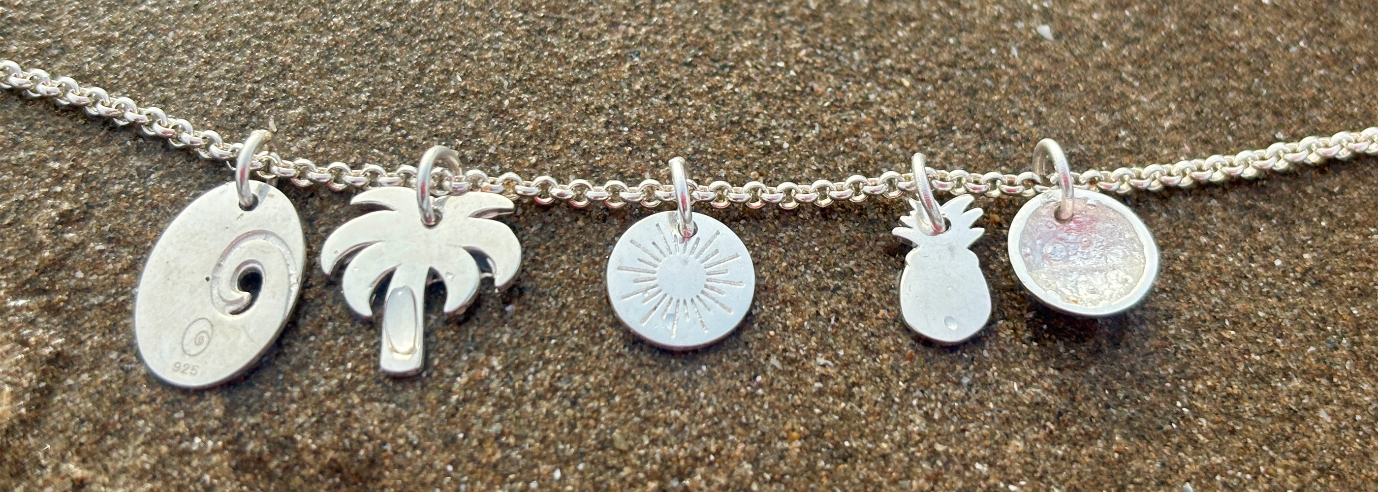 Silver necklace with various charms on a sandy background
