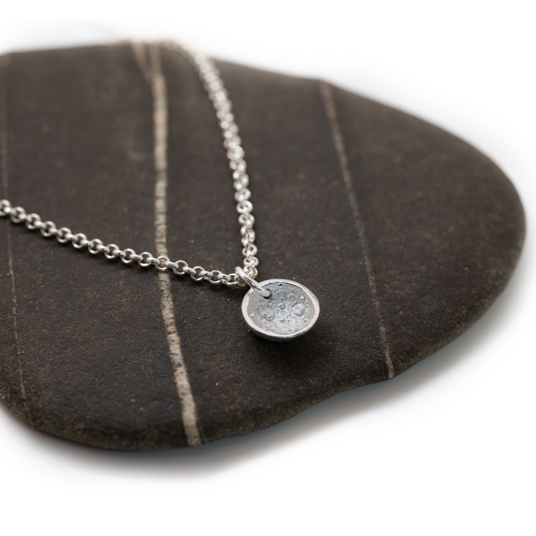 Silver necklace with a round pendant on a dark stone surface