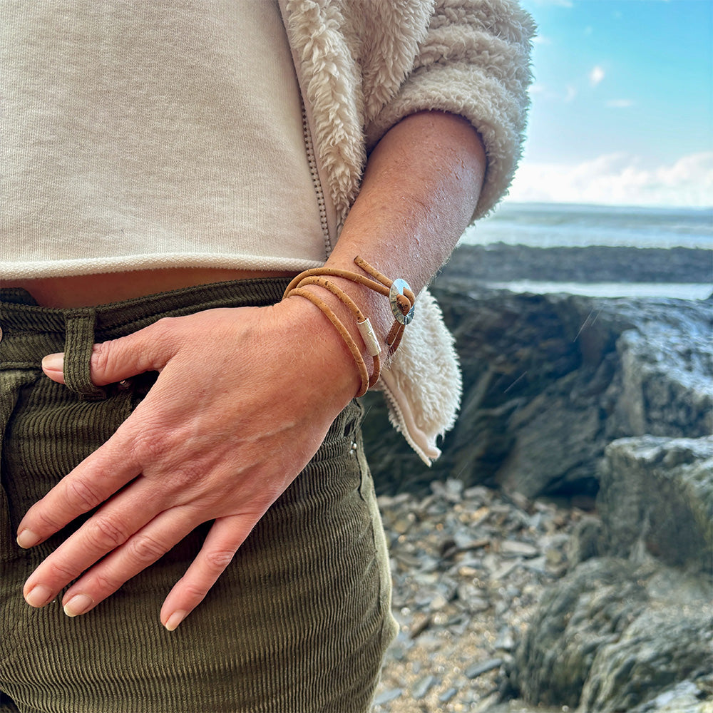 Person at the beach wearing a natural; cork wrap bracelet with silver charms.