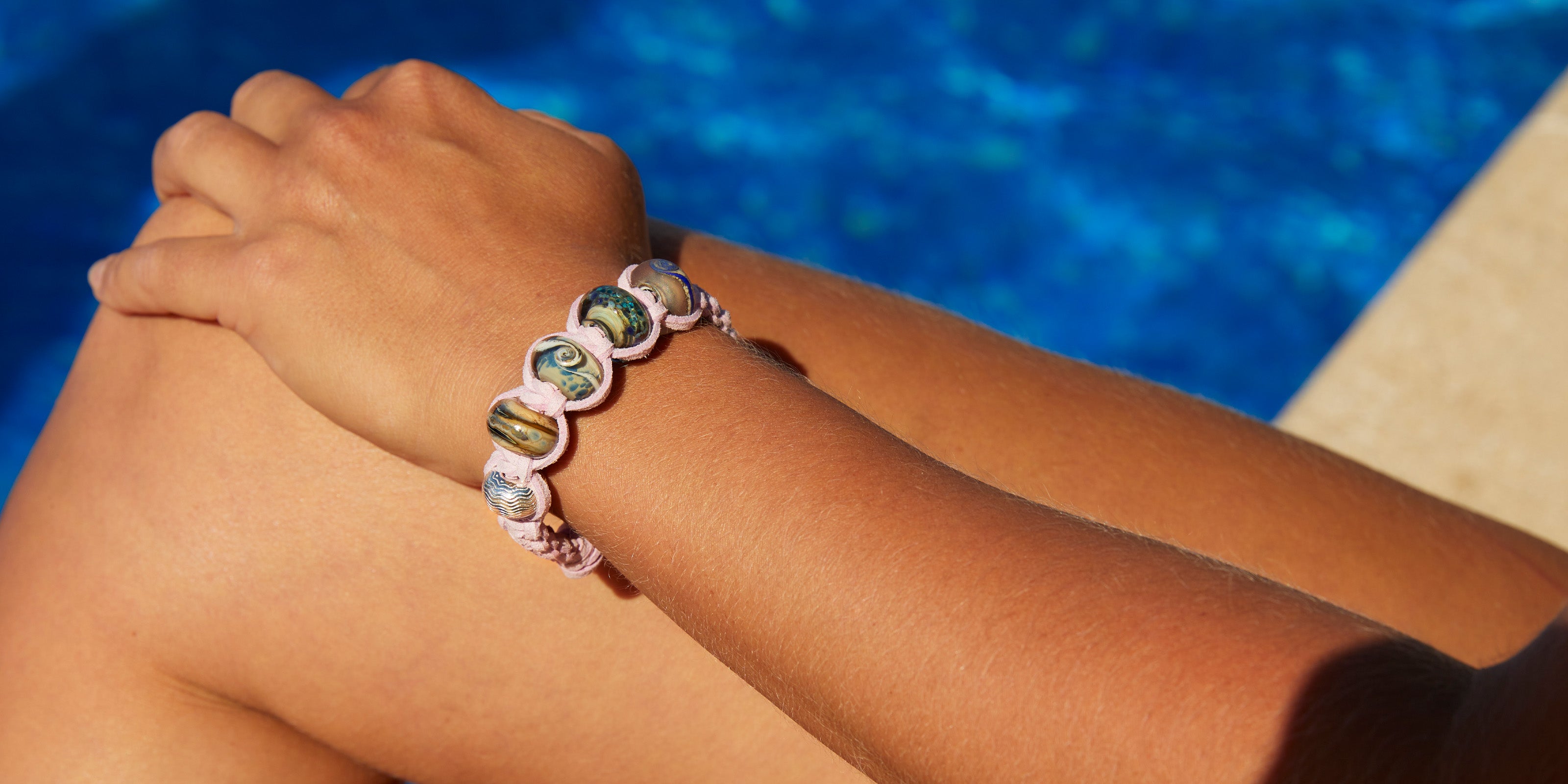 Northumberland beach inspired beads in blue and grey on thistle cord macrame braided bracelet. Worn by woman sitting on the edge of the pool.