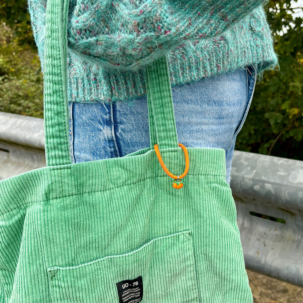 Green corduroy overalls with an orange button, worn by a person, with a blurred natural background.