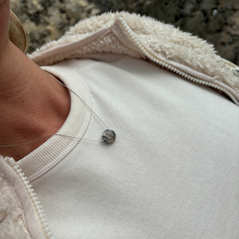Person wearing a white t-shirt wearing a sandy bead pendant necklace.