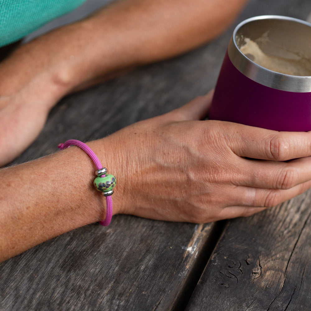 Person holding a purple insulated mug with a pink bracelet on a wooden surface