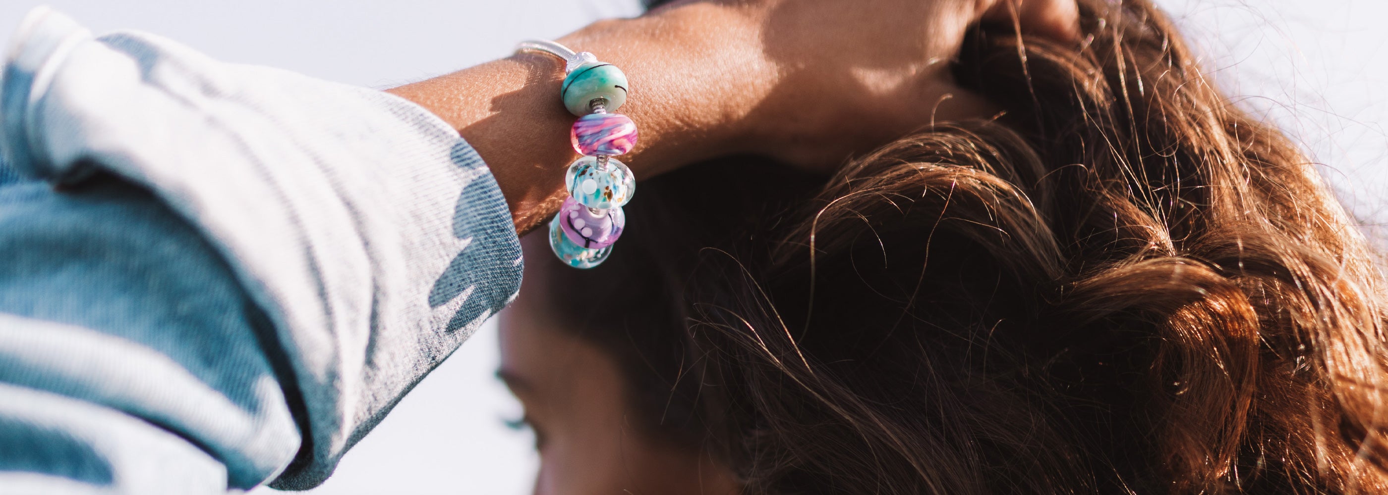Pink, blue and green murano glass beads worn on silver bracelet, girl wearing denim jacket.