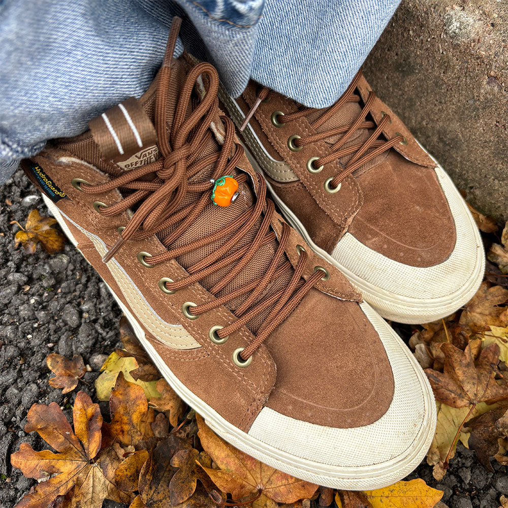 Brown high-top sneakers with white soles on a leaf-covered ground