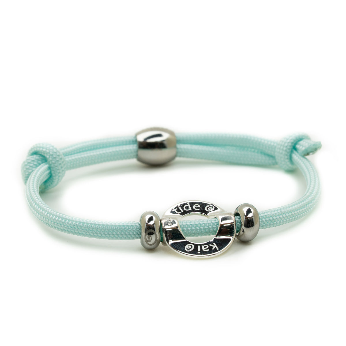 A light mint green braided cord bracelet with polished silver-tone metal beads and a central oval charm engraved with 'kai' and 'tide'.