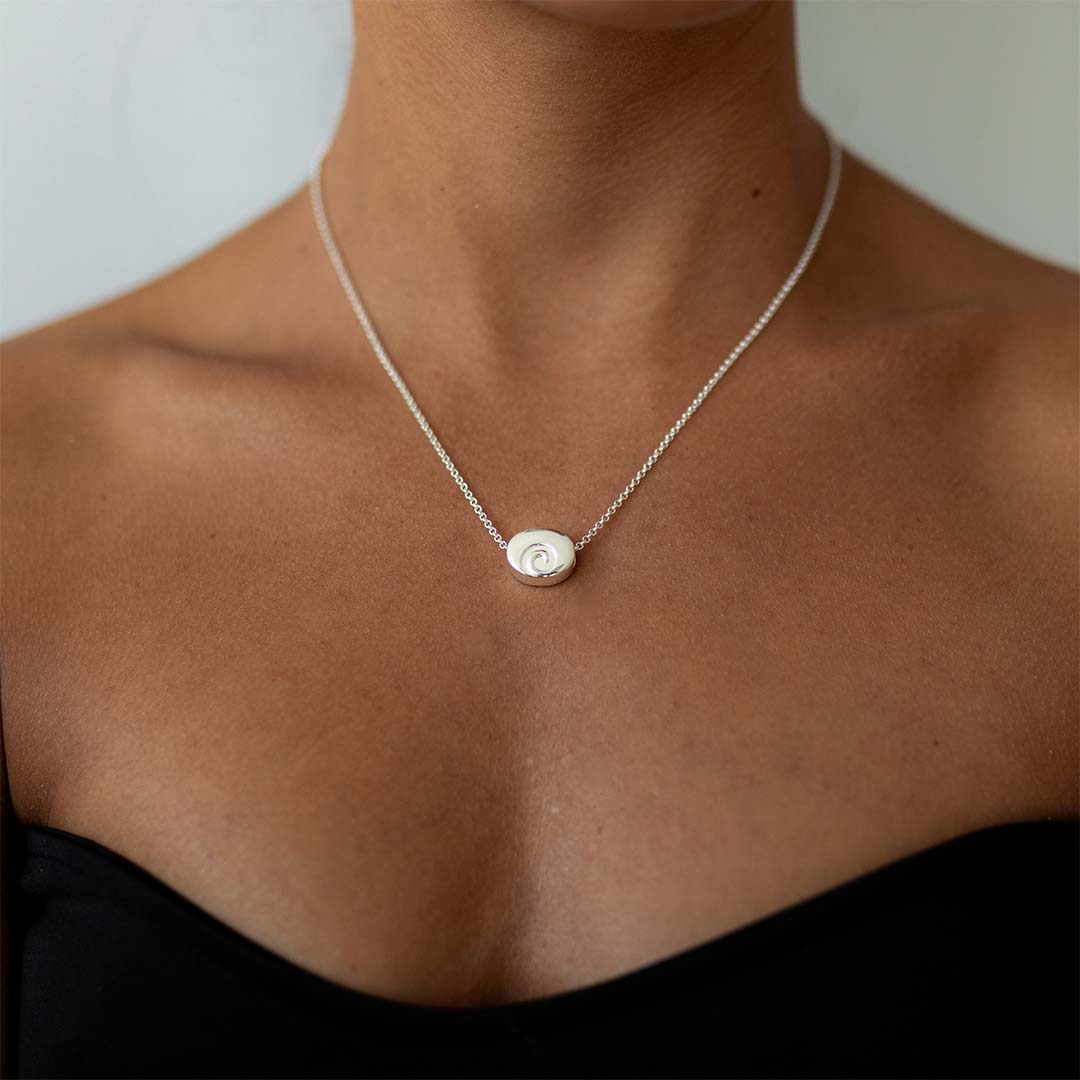 Woman wearing a silver necklace with the silver swirl charm on it.