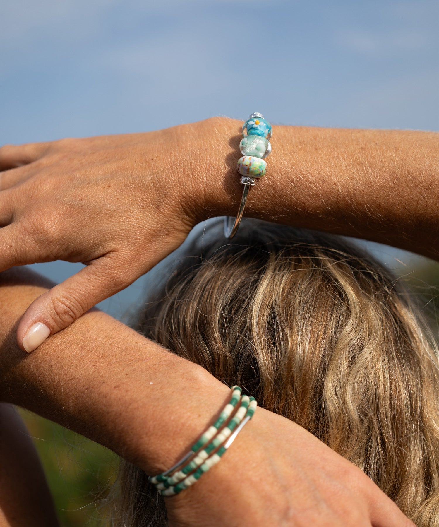 Close-up of a person's wrist with two beaded bracelets against a blurred natural background
