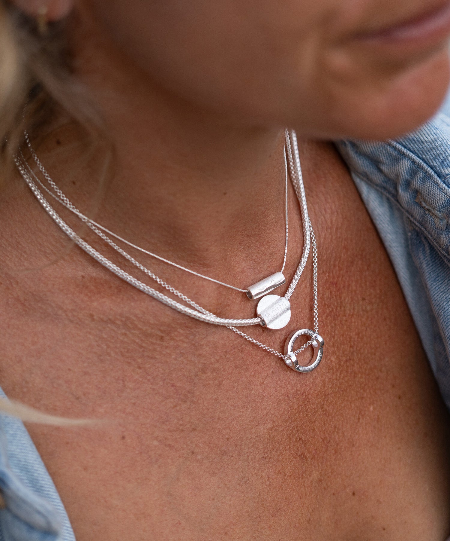 Close-up of a person wearing multiple silver necklaces with circular pendants.