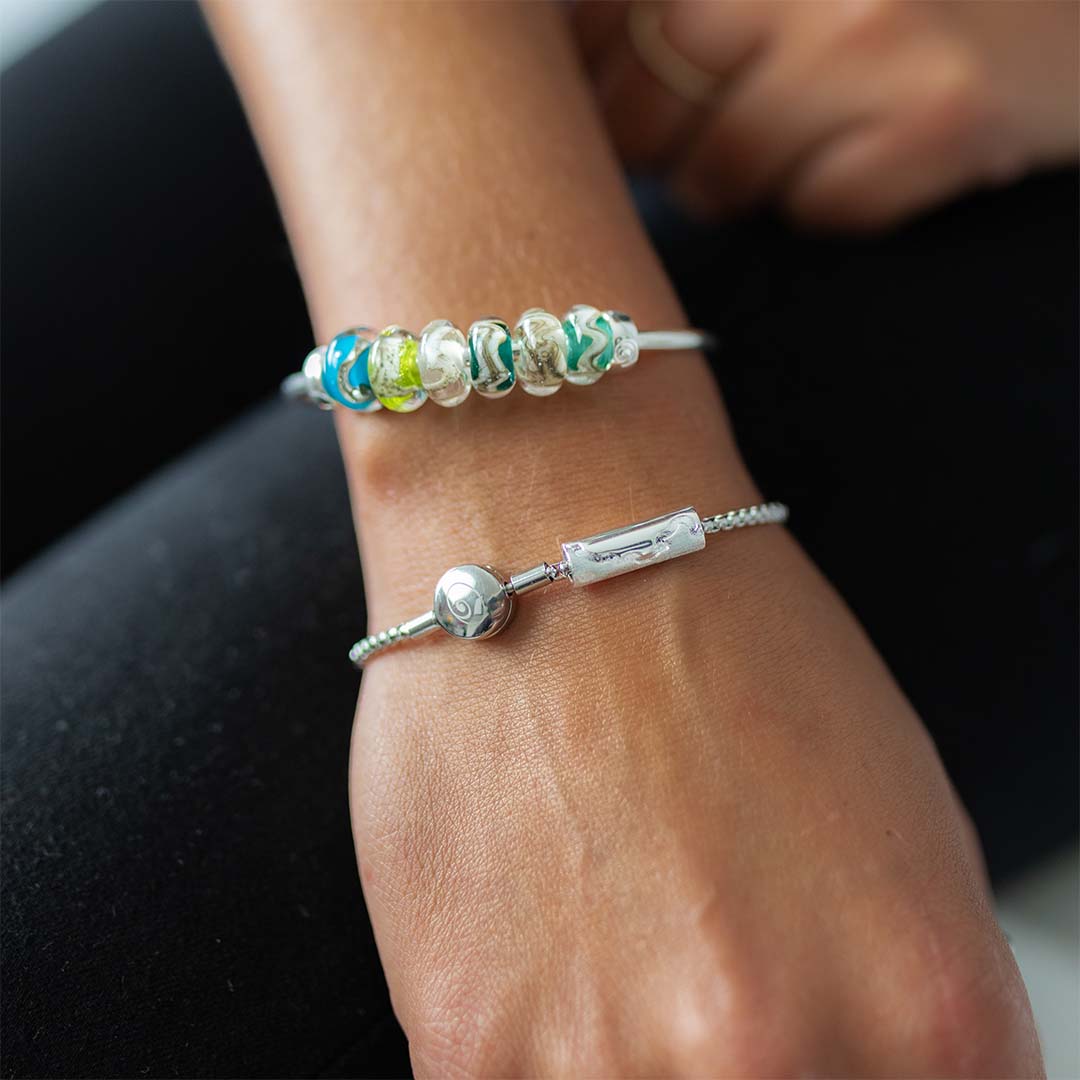 Person wearing a silver bead bangle and bracelet with silver charm.