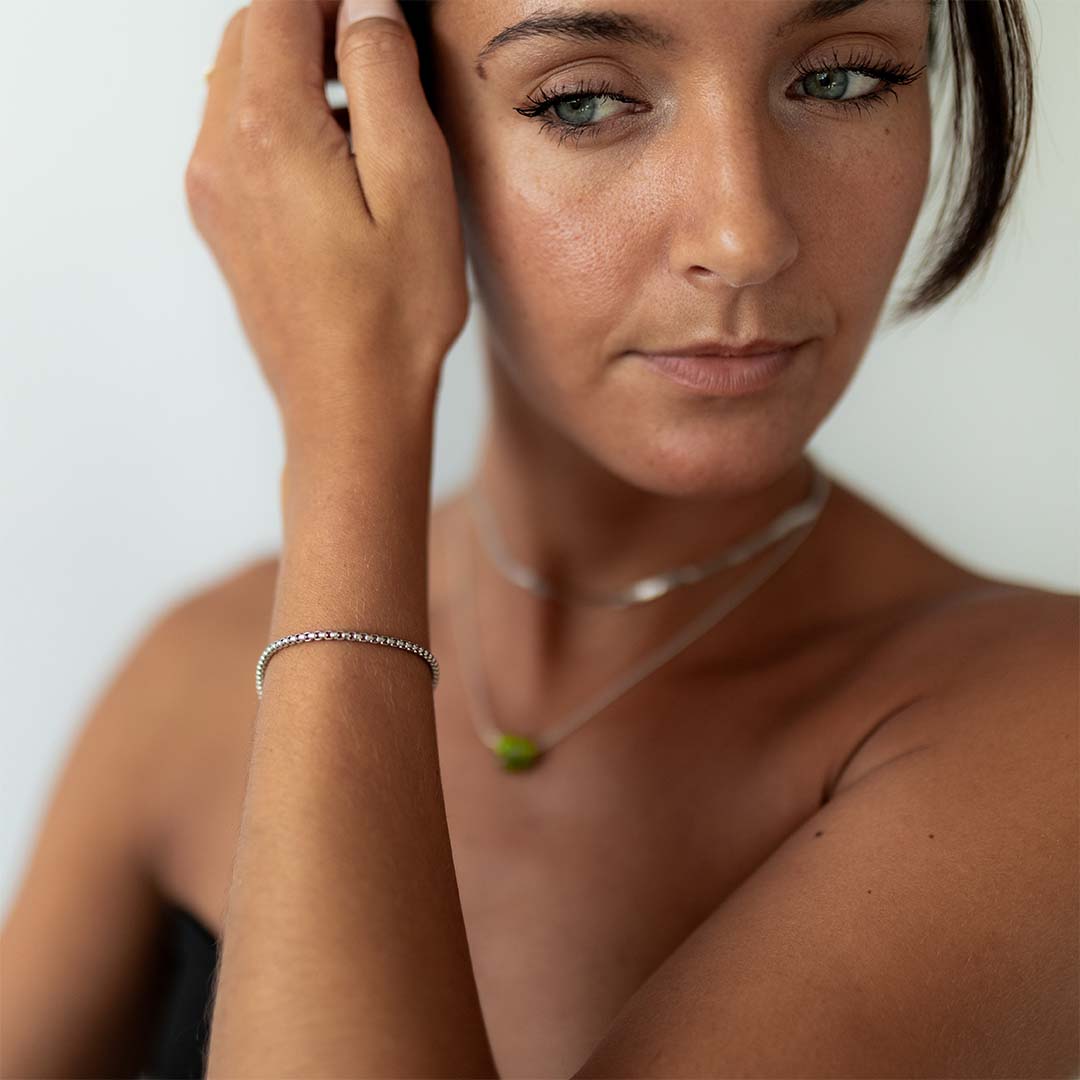 Woman wearing a silver chain bracelet and necklace, pushing her hair back.