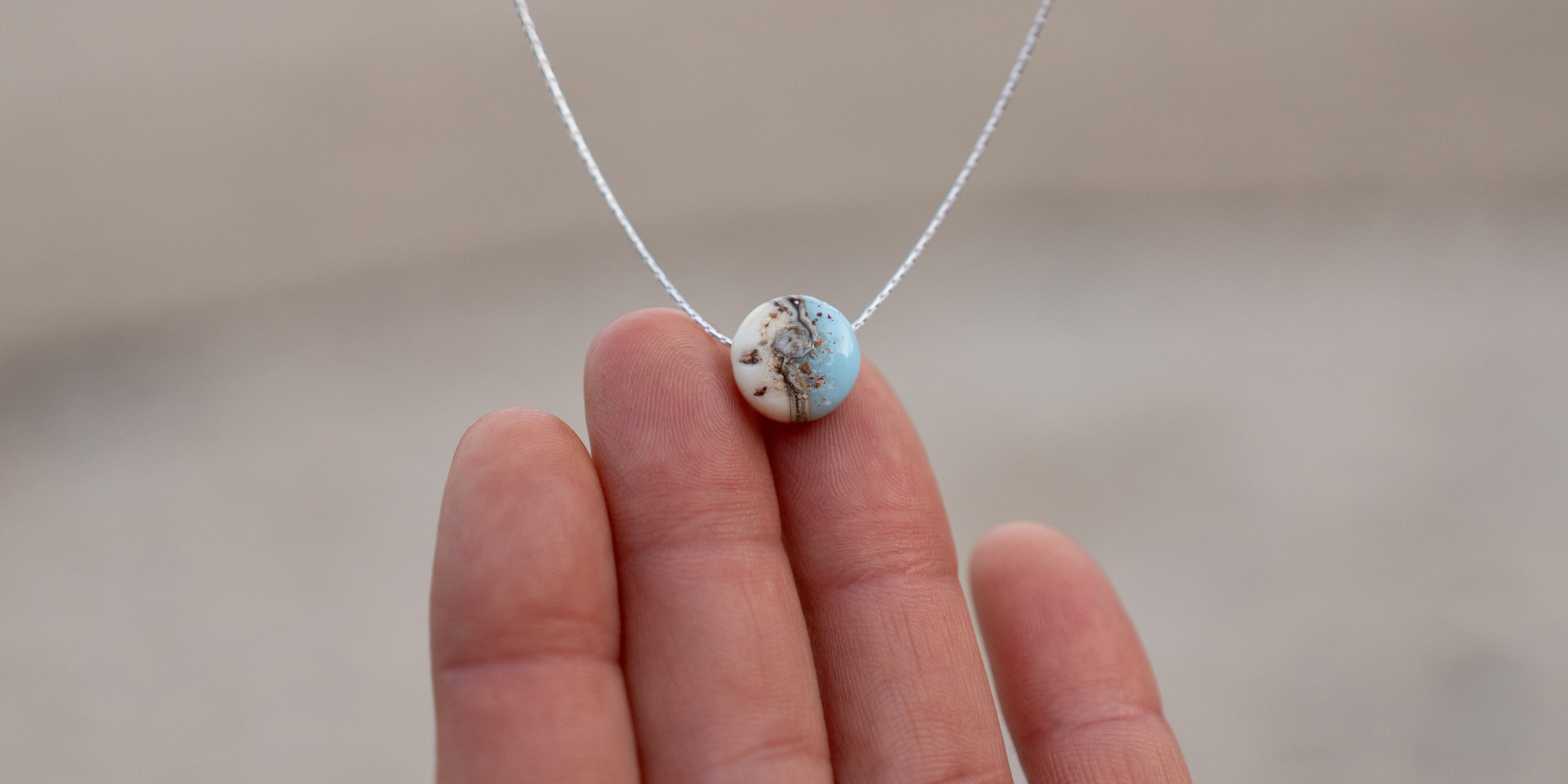 Necklace with a round pendant held between two fingers against a neutral background