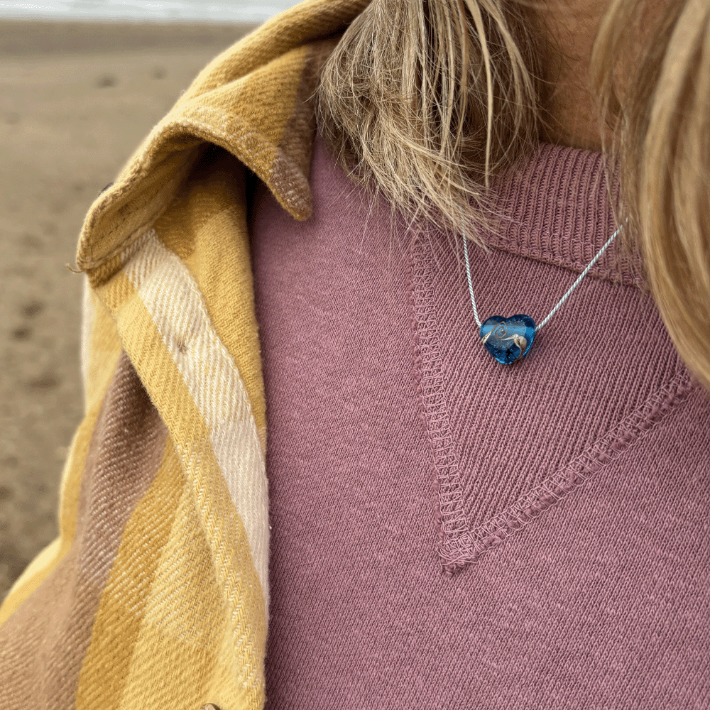 Person wearing a purple sweater and yellow coat with a blue heart pendant necklace.