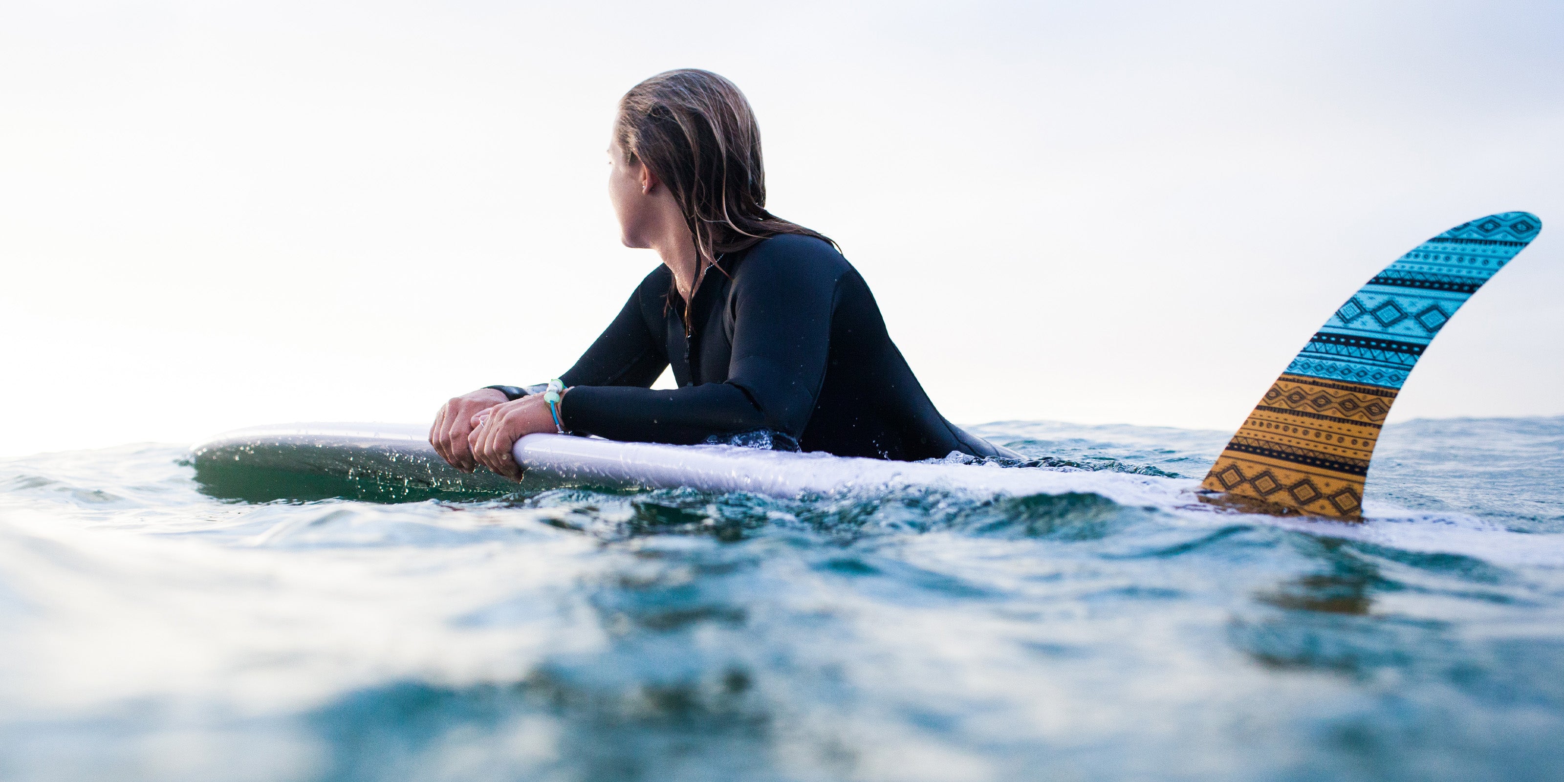 Woman on surfboard in the sea wearing silver nalu beads bracelet.