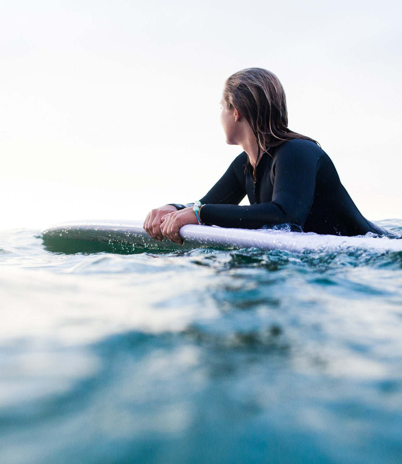 Woman on surfboard in the sea wearing silver nalu beads bracelet.