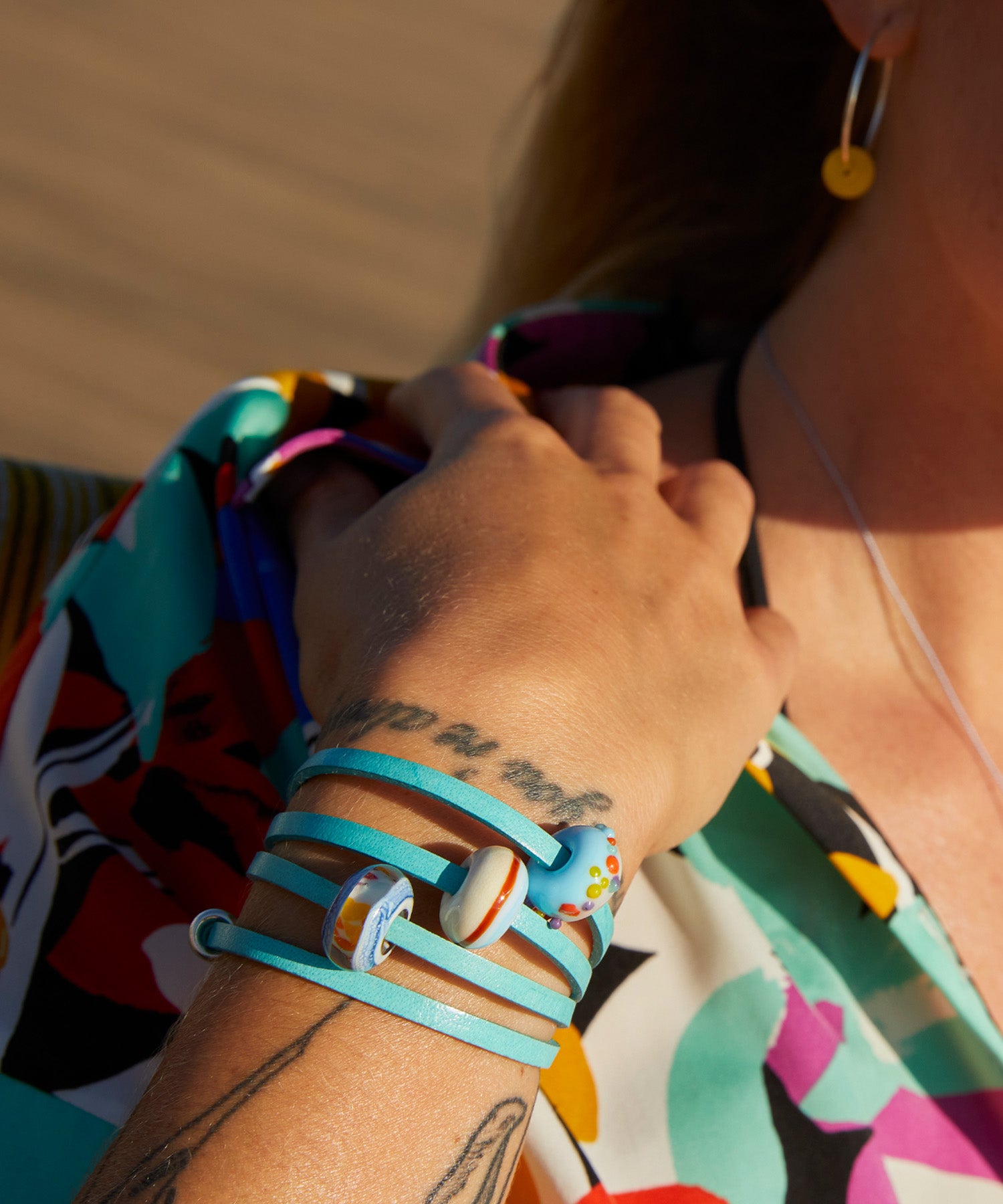 Woman in a colourful beach shirt wearing a turquoise leather wrap bracelet with glass beads.