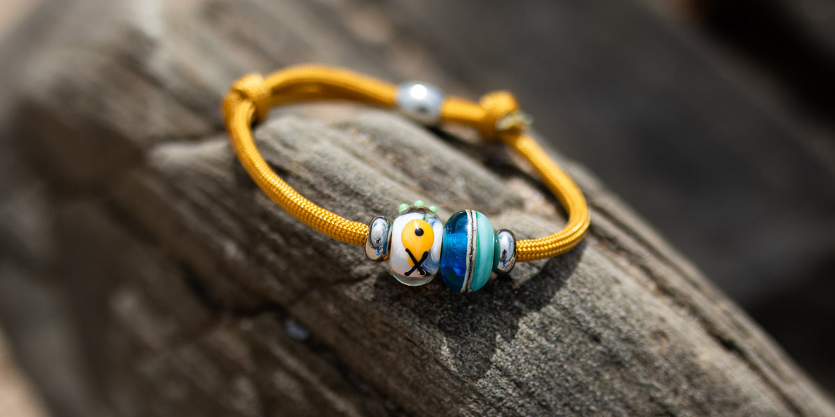 Yellow cord bracelet with blue, white and yellow glass beads on a natural background.