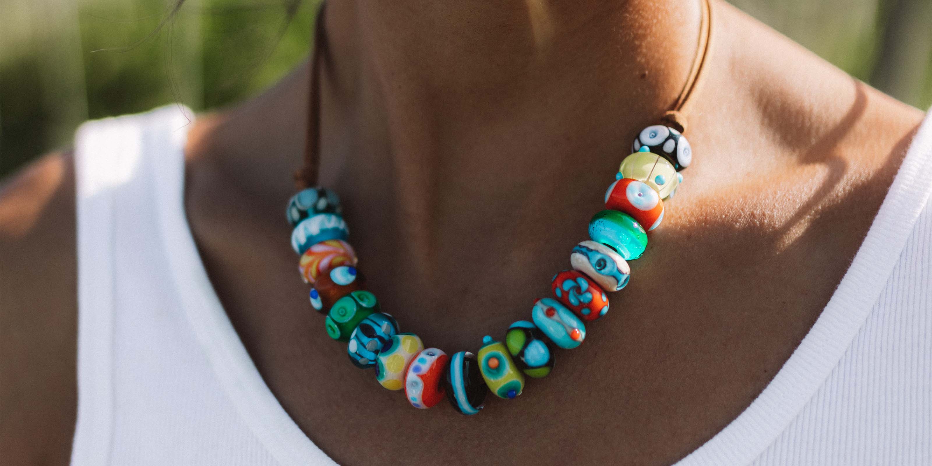 Multicolour glass beads strung on cord necklace worn by surf girl at the beach.