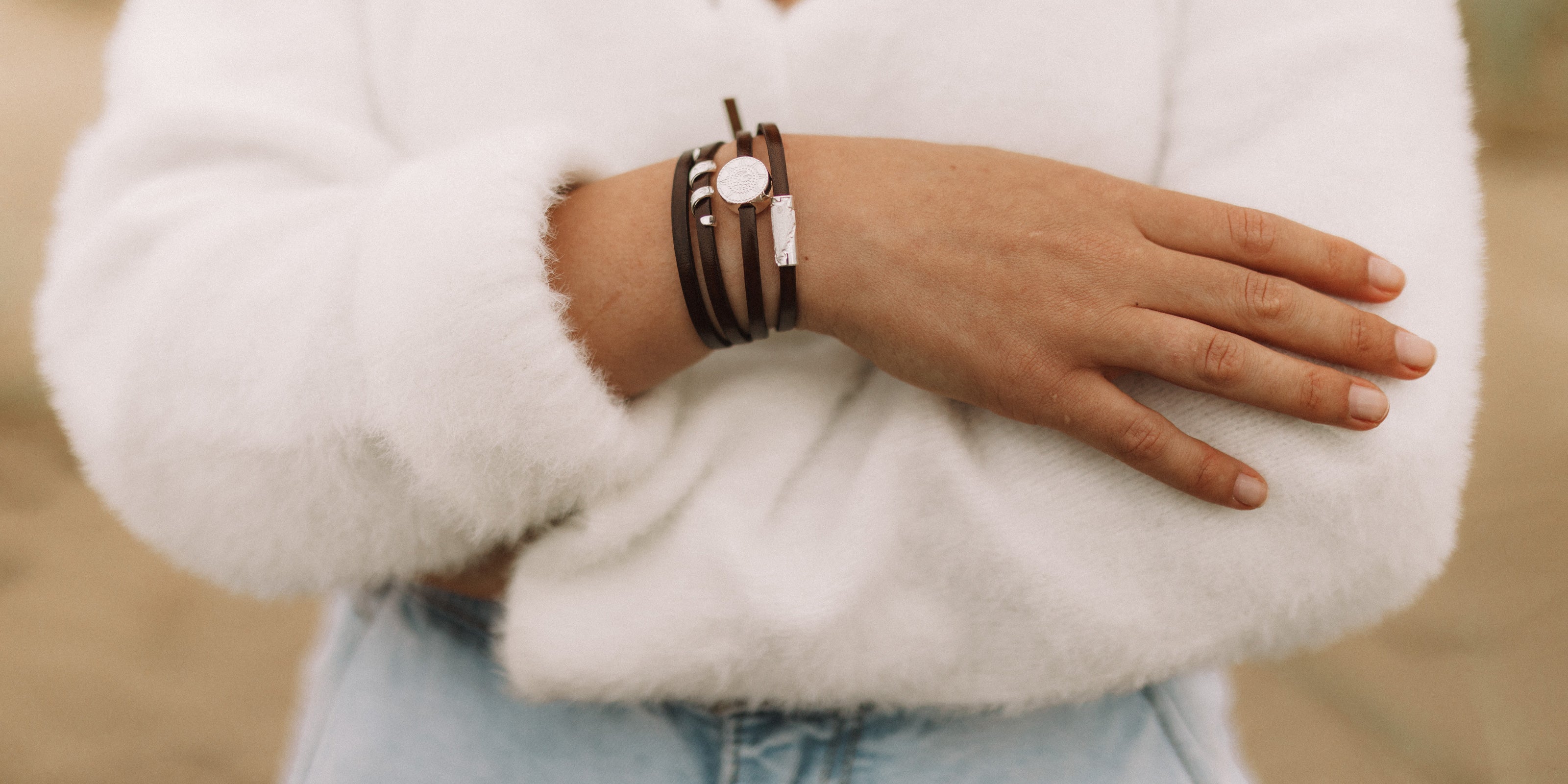 Silver beads on brown leather wrap bracelet worn by woman on the beach.