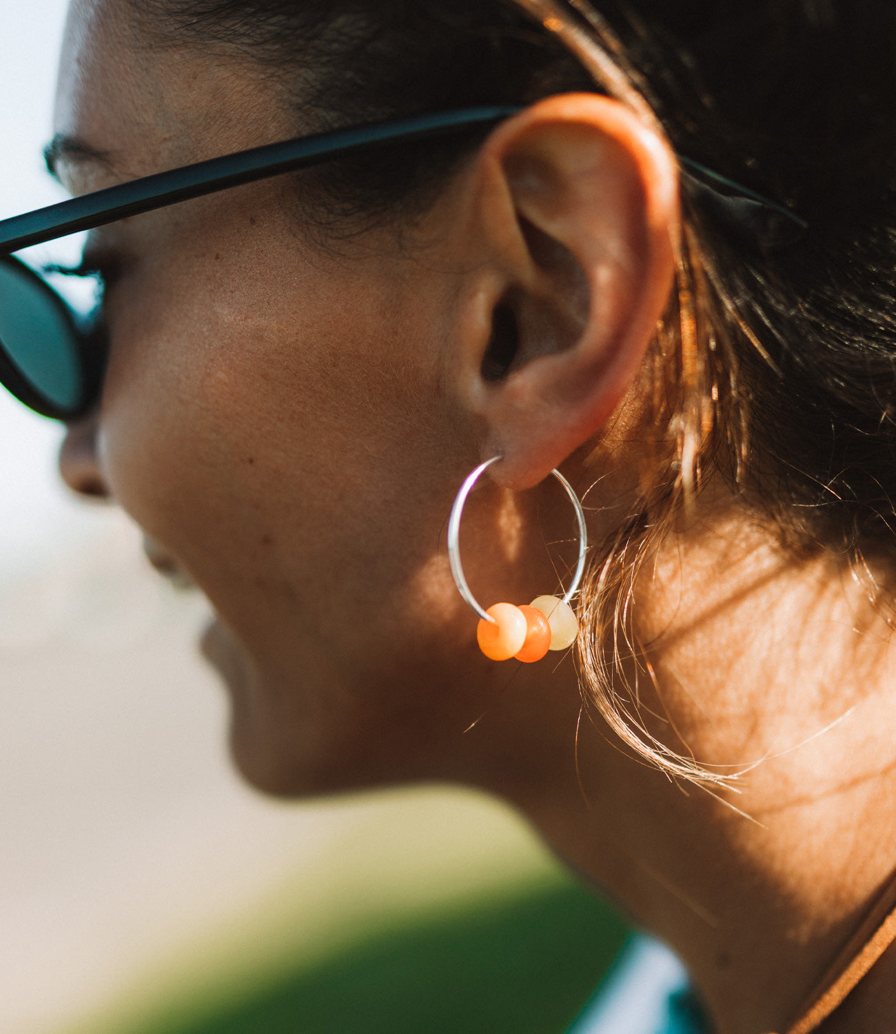 Orange and green beads on silver hoop earrings worn by woman wearing sunglasses.