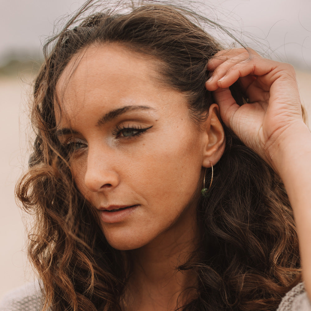 Lady wearing gold earrings with little beads made with grains of sand from beaches.