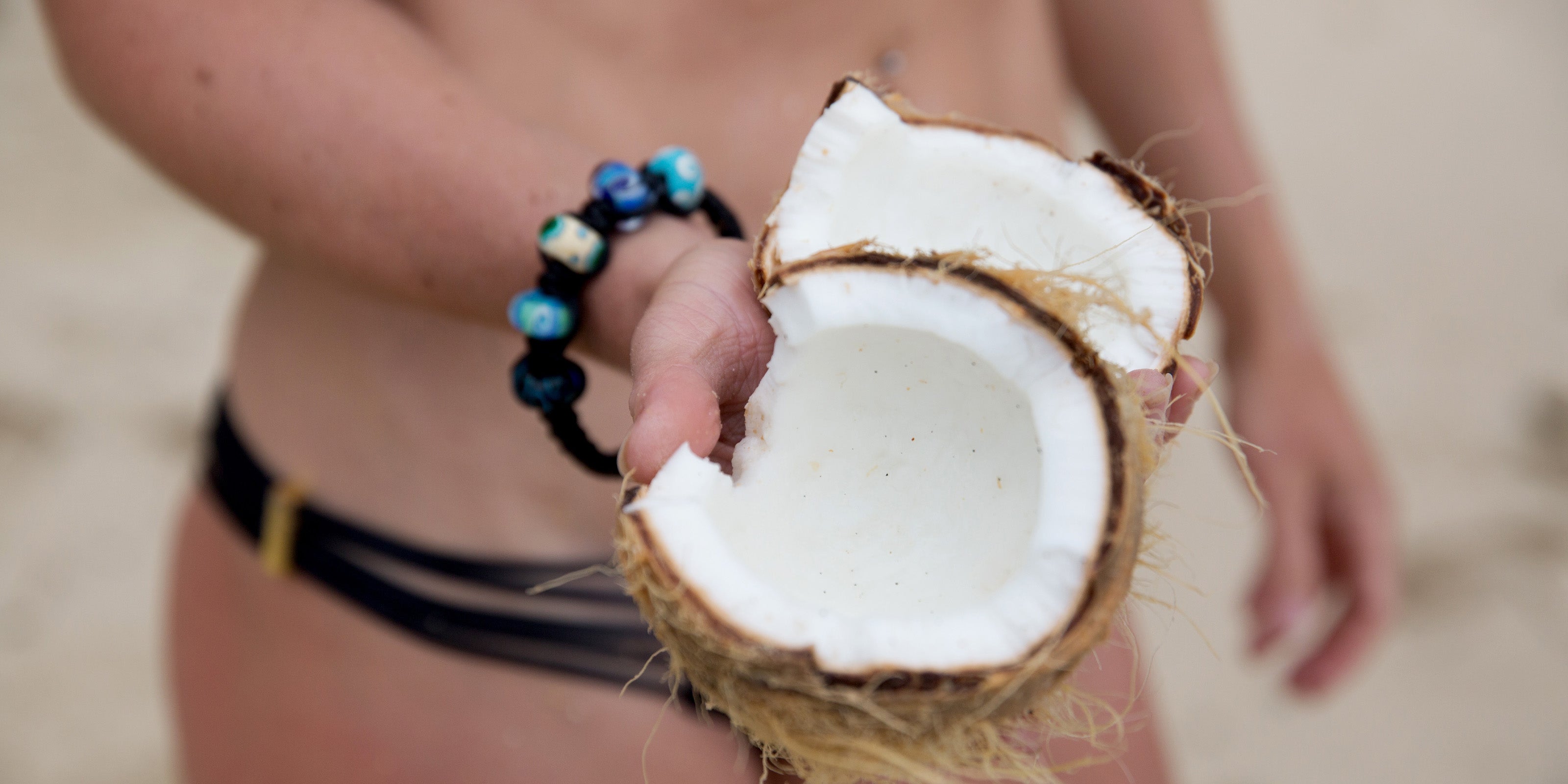 Coconut being held by lady in bikini wearing black island bead bracelet.