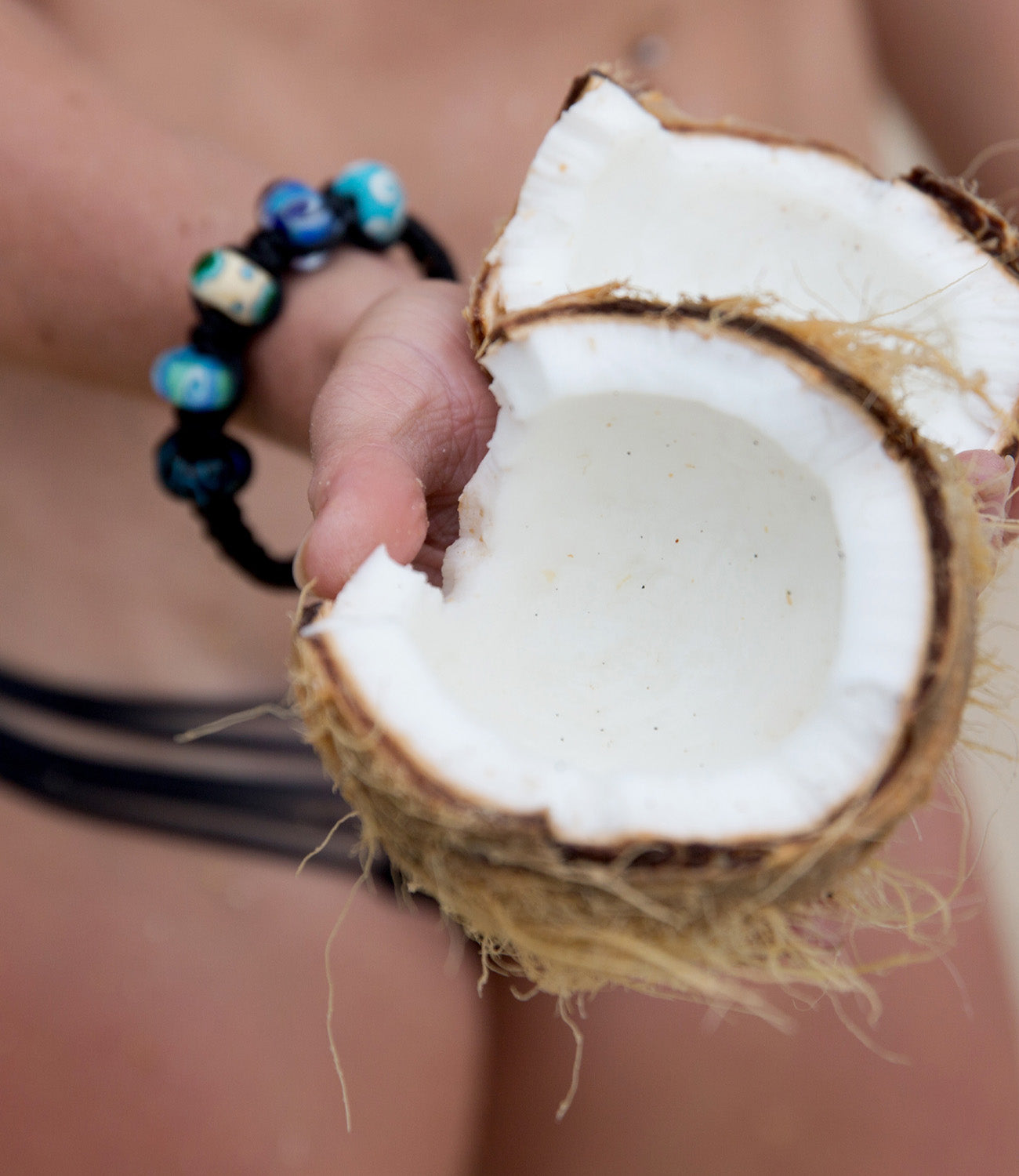 Coconut being held by lady in bikini wearing black island bead bracelet.