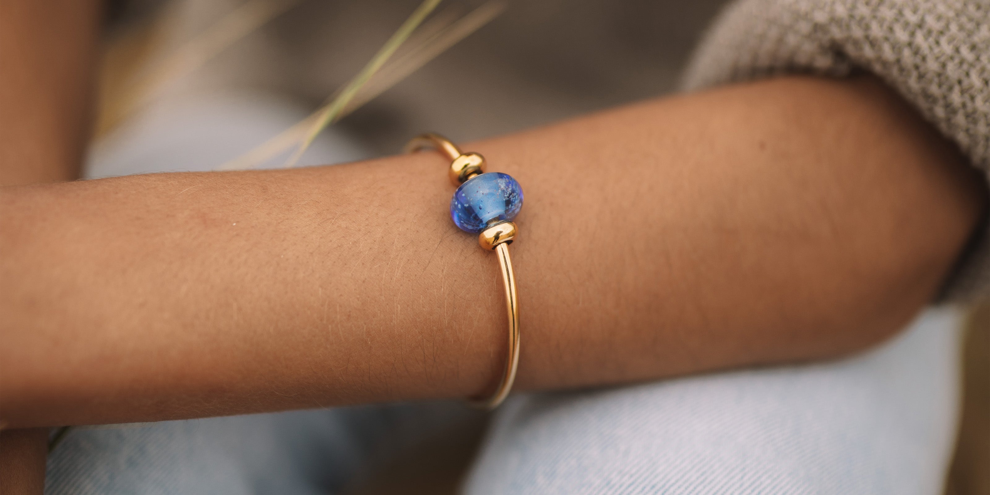 Gold bangle with dark blue sand bead worn by girl on beach.
