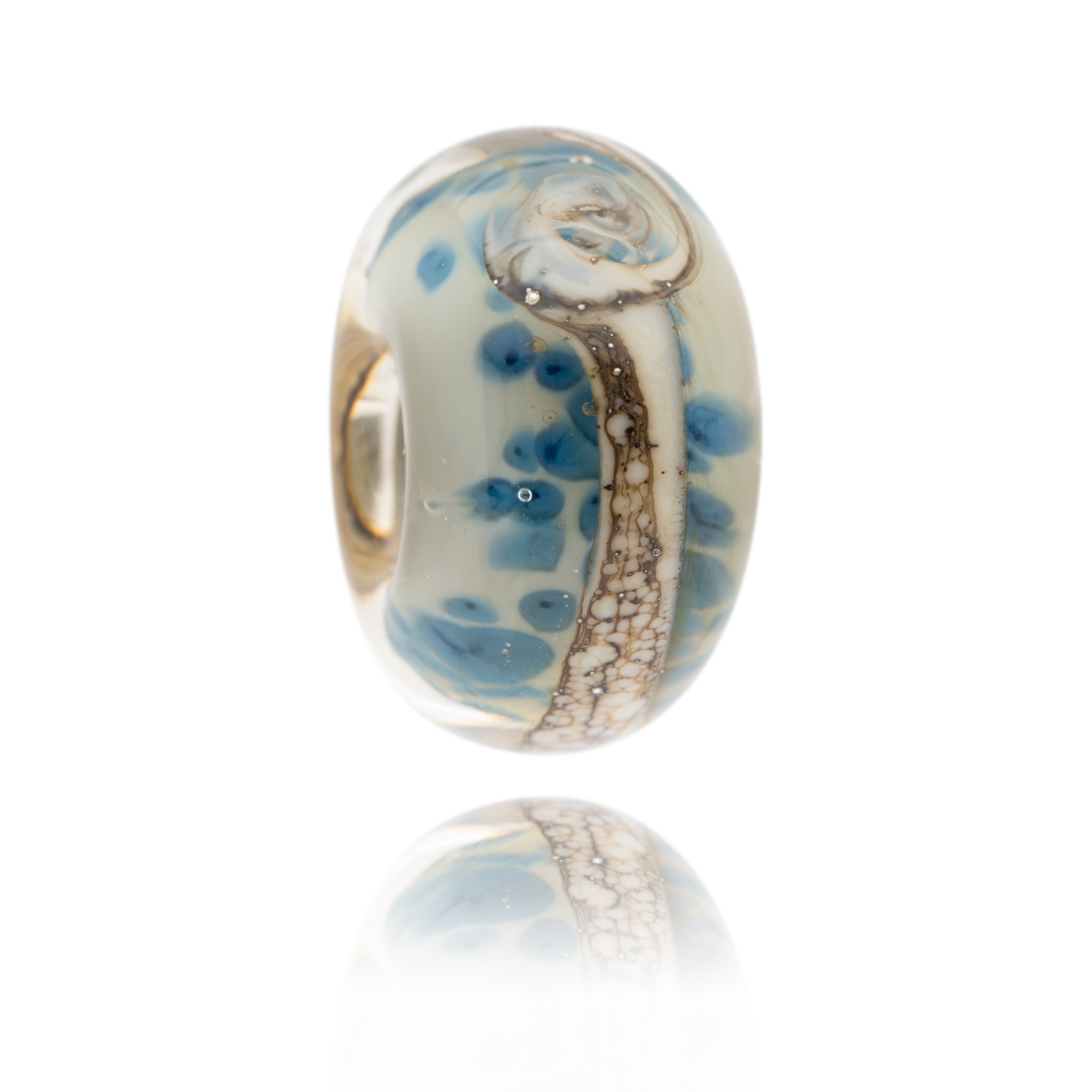 Cream glass bead with dark blue patterns within the glass. This bead represents Bamburgh Beach in Northumberland.