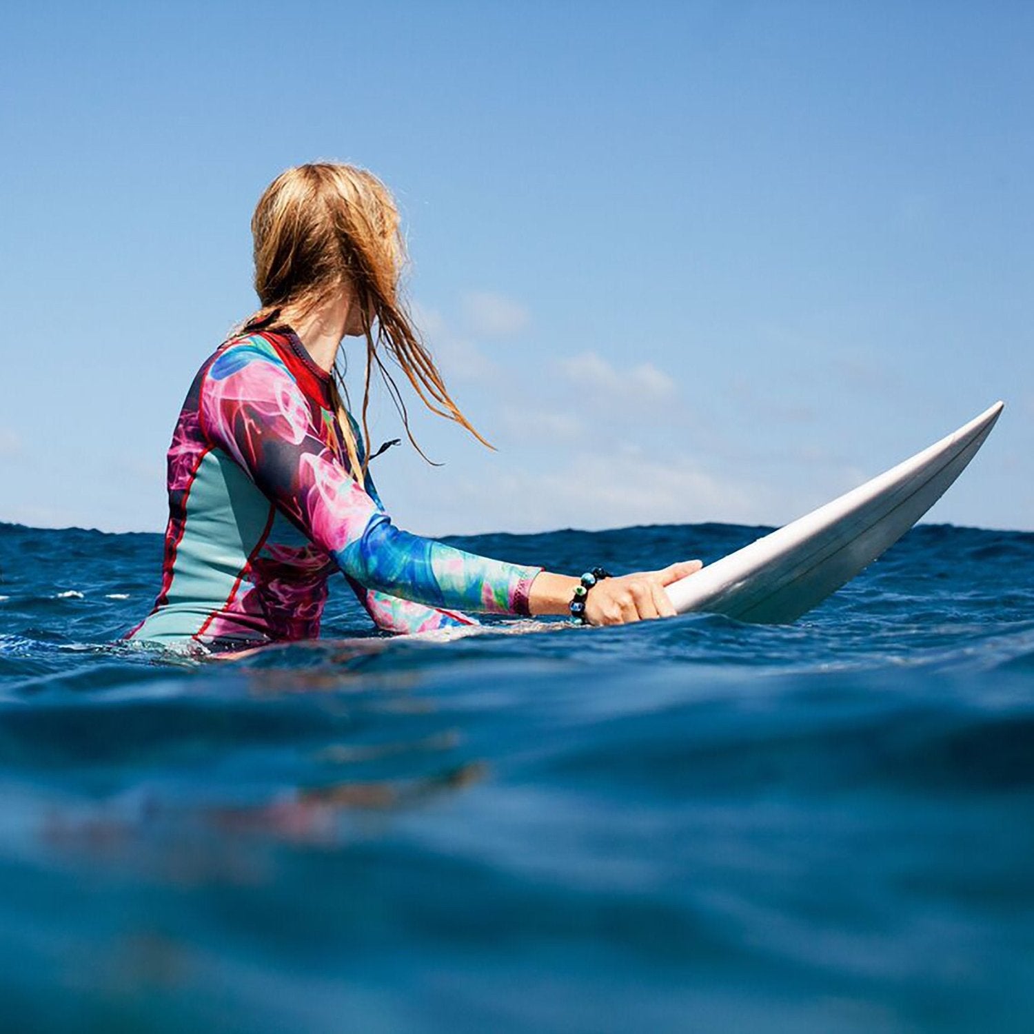 Surfer girl with bright colourful wetsuit on her surfboard, sitting in the sea.