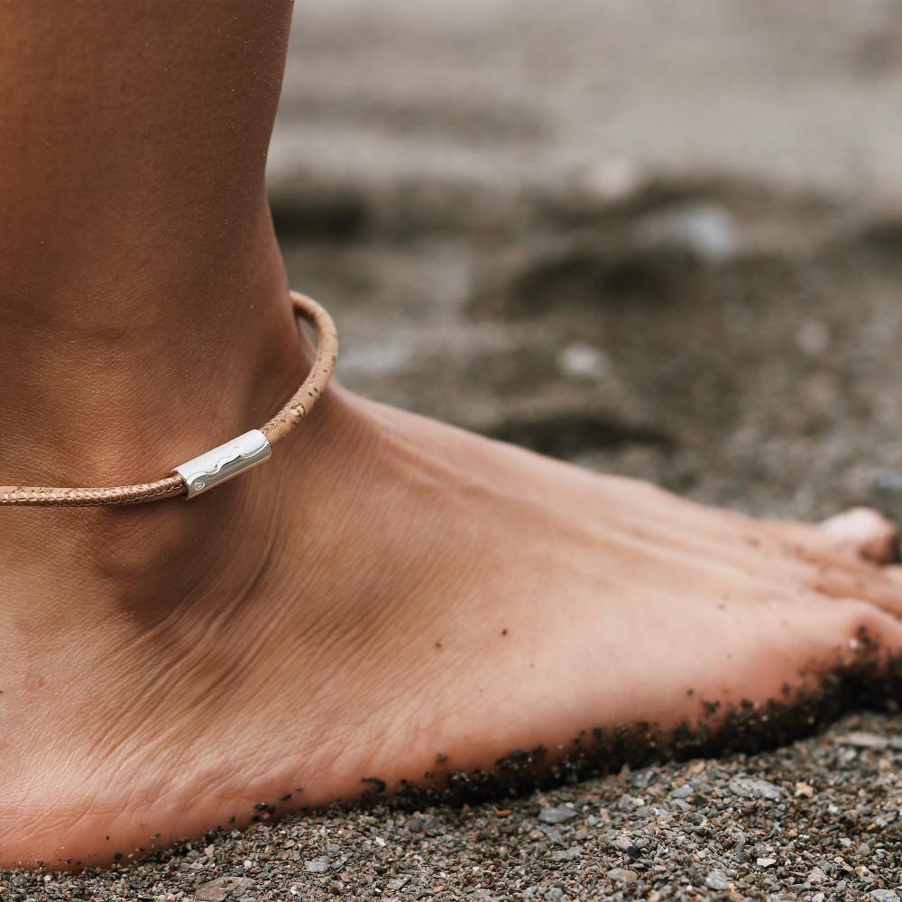 Person wearing a cork anklet with silver tube charm on it.