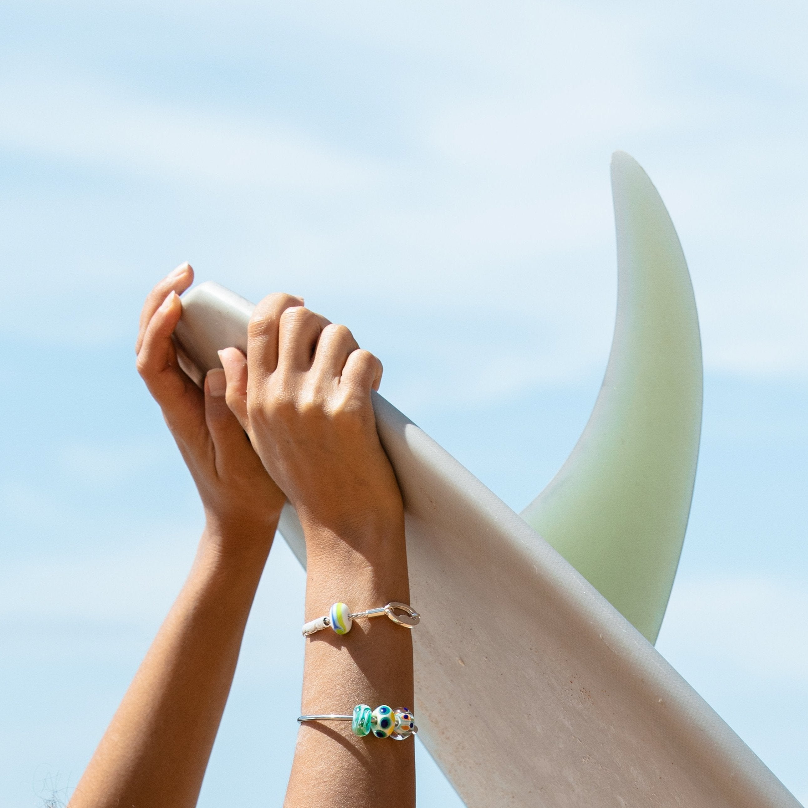Hands holding surfboard up in the air.