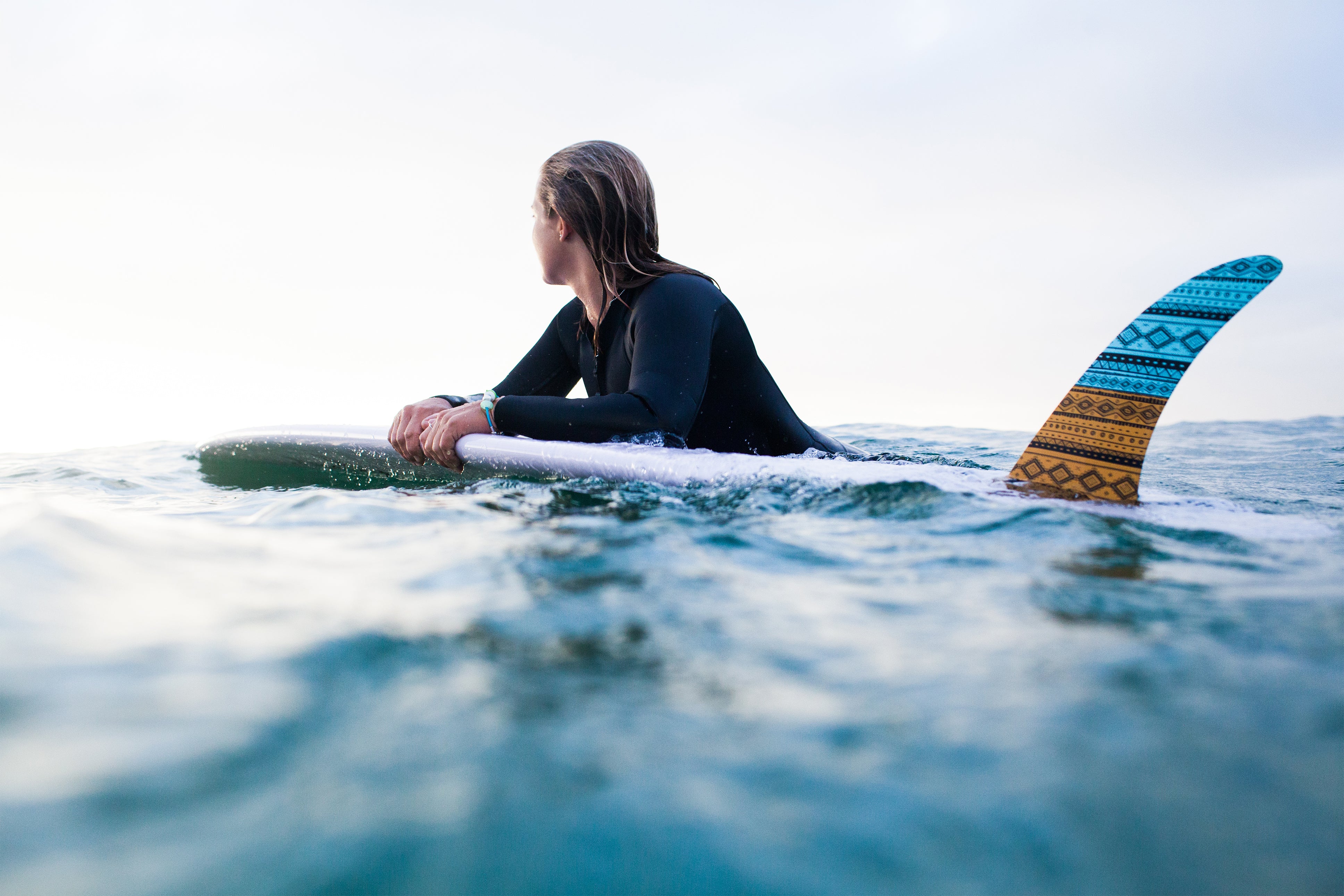 Sea inspired jewellery and beads on turquoise rubber bracelet worn by women surfer with longboard.