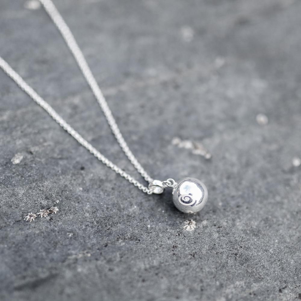 Silver chime ball necklace on stone at the beach.