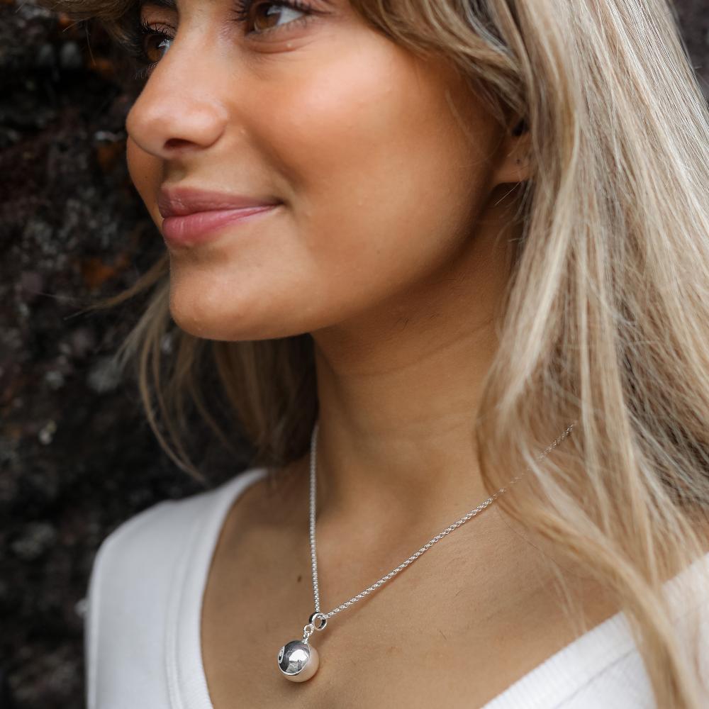 Woman wearing a white top and silver chime ball necklace.